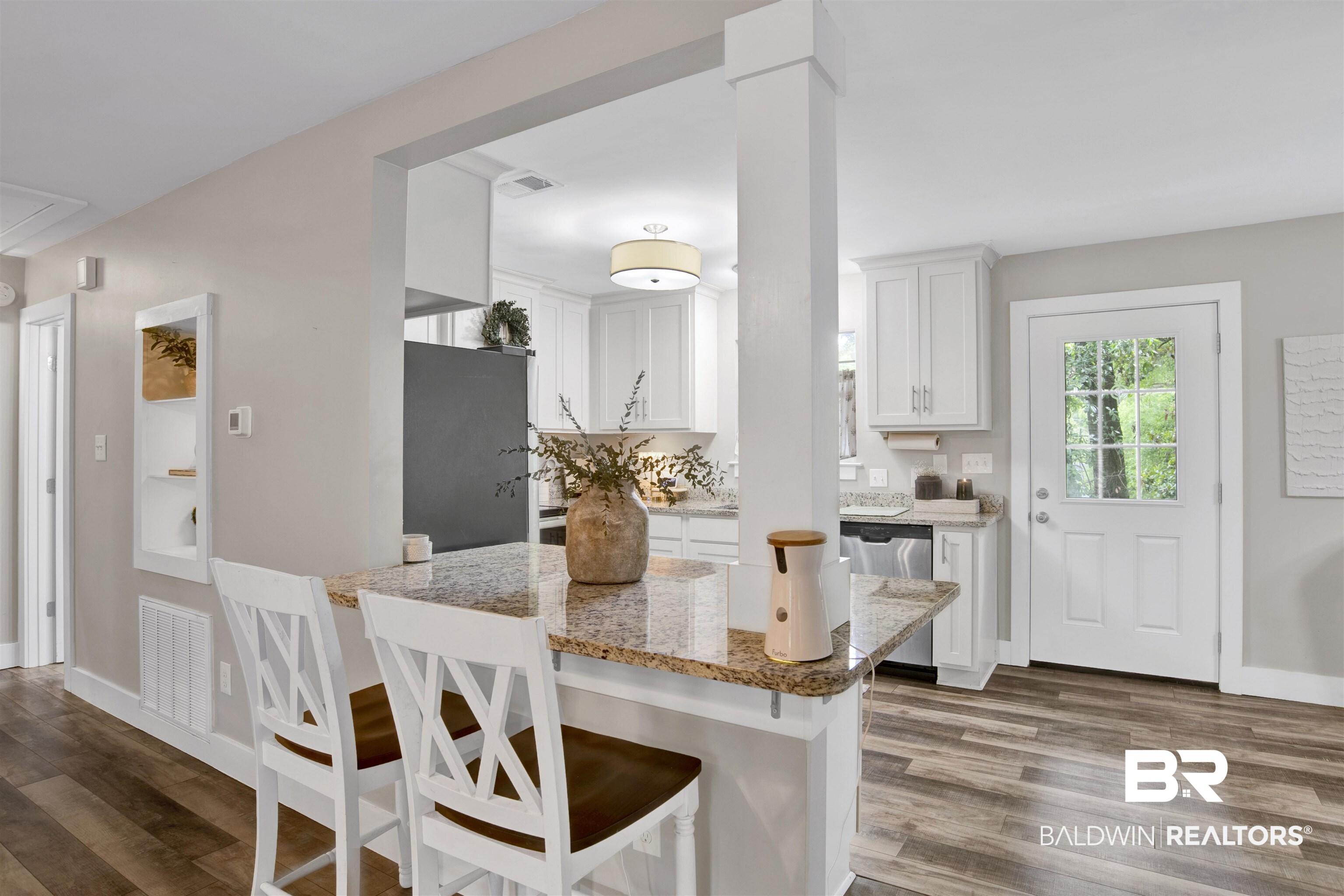 Image 4: Kitchen featuring a granite countertop peninsula, built-in white cabinetry, stainless steel dishwasher, and a white paneled door with windowpanes