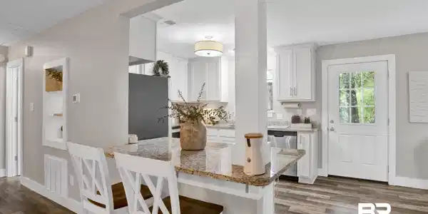Image 4: Kitchen featuring a granite countertop peninsula, built-in white cabinetry, stainless steel dishwasher, and a white paneled door with windowpanes