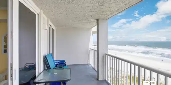 Image 3: Spacious balcony with a painted concrete floor and a white metal railing, offering expansive views of the sandy beach and ocean