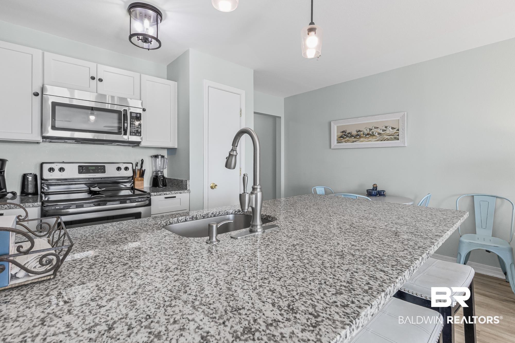 Image 2: Kitchen featuring stainless steel appliances, light stone countertops, white cabinetry, hanging light fixtures, and a breakfast bar