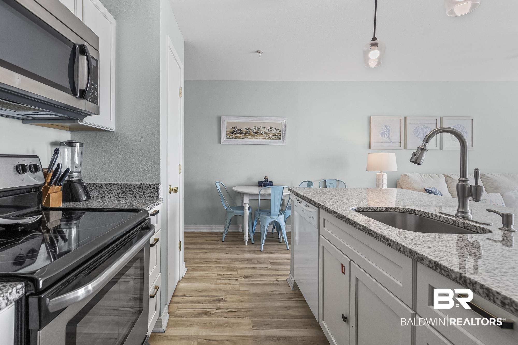 Image 3: Kitchen with stainless steel appliances, white cabinetry, light stone countertops, pendant lighting, and light wood-style floors