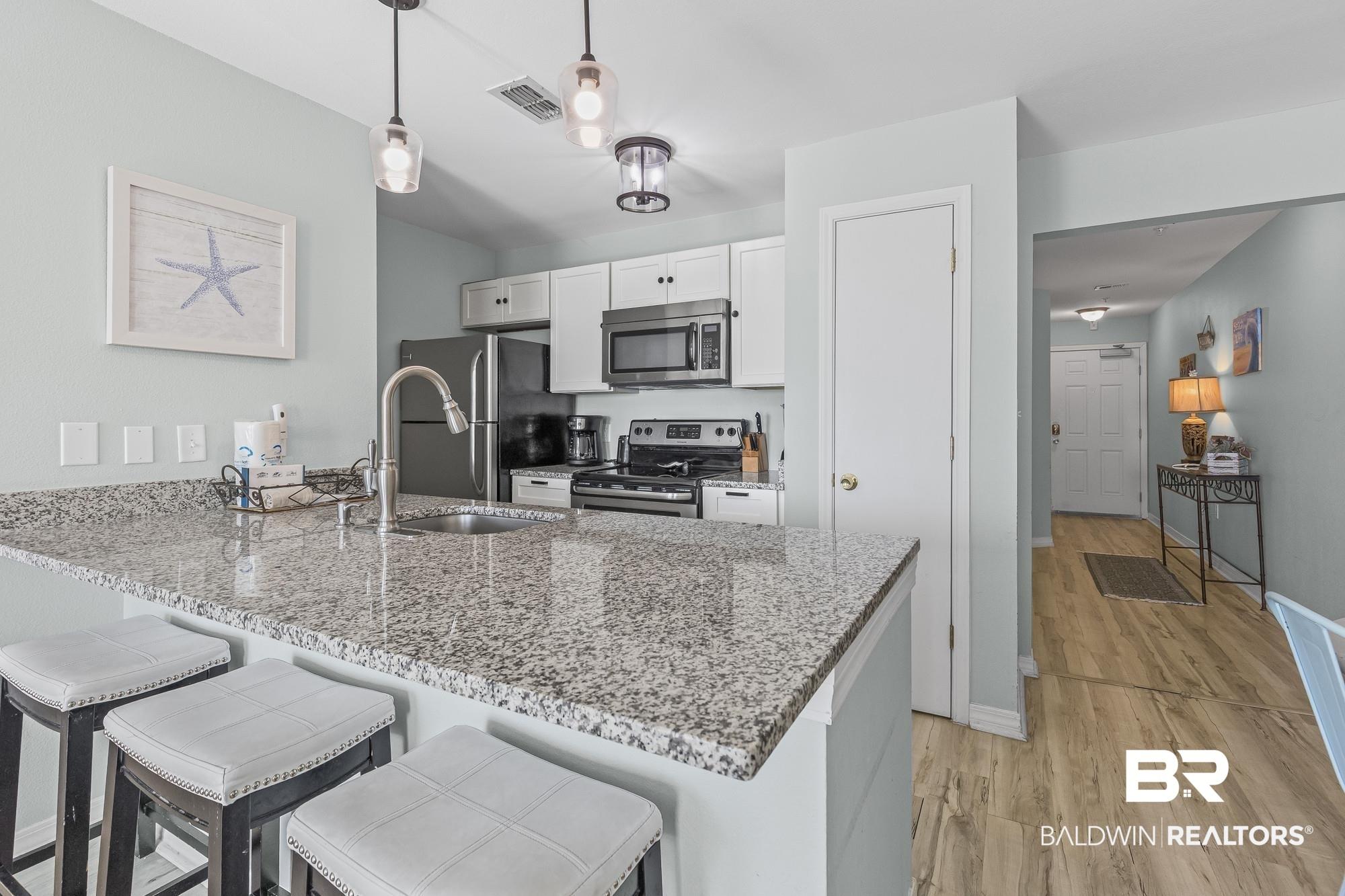 Image 4: Kitchen featuring a breakfast bar area, stainless steel appliances, a peninsula, light stone counters, and white cabinets