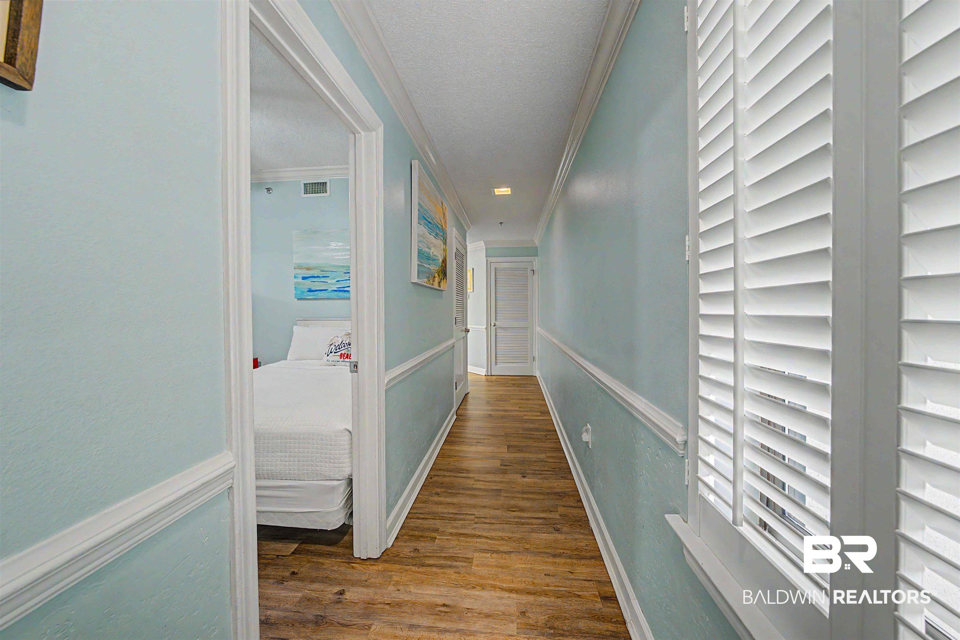 Image 4: Hallway with wood-finish flooring, light blue walls, and white plantation shutters