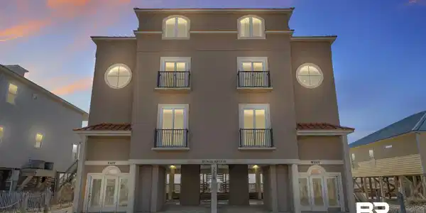 Image 2: Back of house at dusk with french doors, a balcony, and stucco siding
