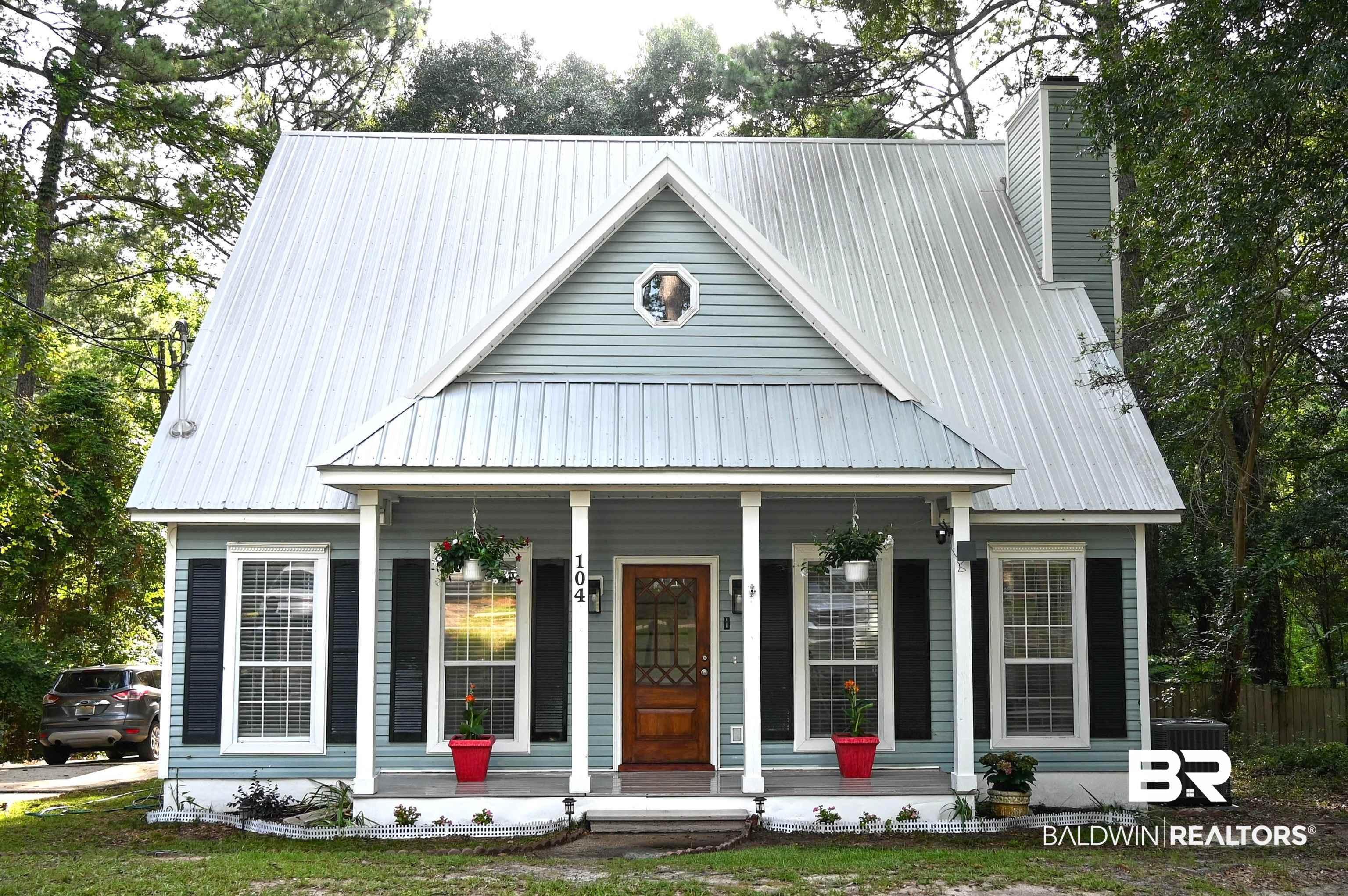 Image 1: Light blue siding exterior featuring a metal roof, front porch with white columns, dark wood-finish front door with glass panels, and black window shutters
