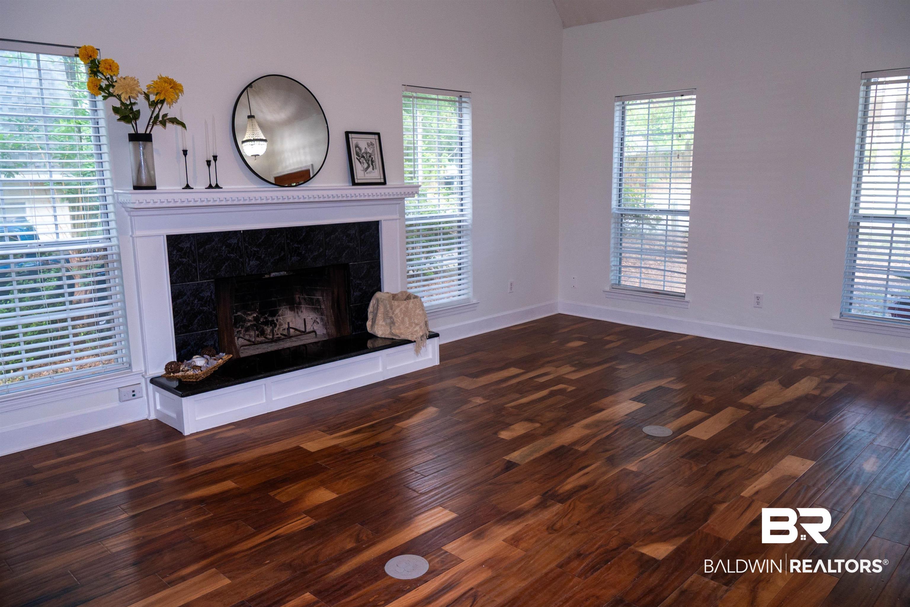 Image 2: Spacious room featuring vaulted ceilings, a prominent fireplace with a white mantel and dark tile surround, and rich wood-finish flooring