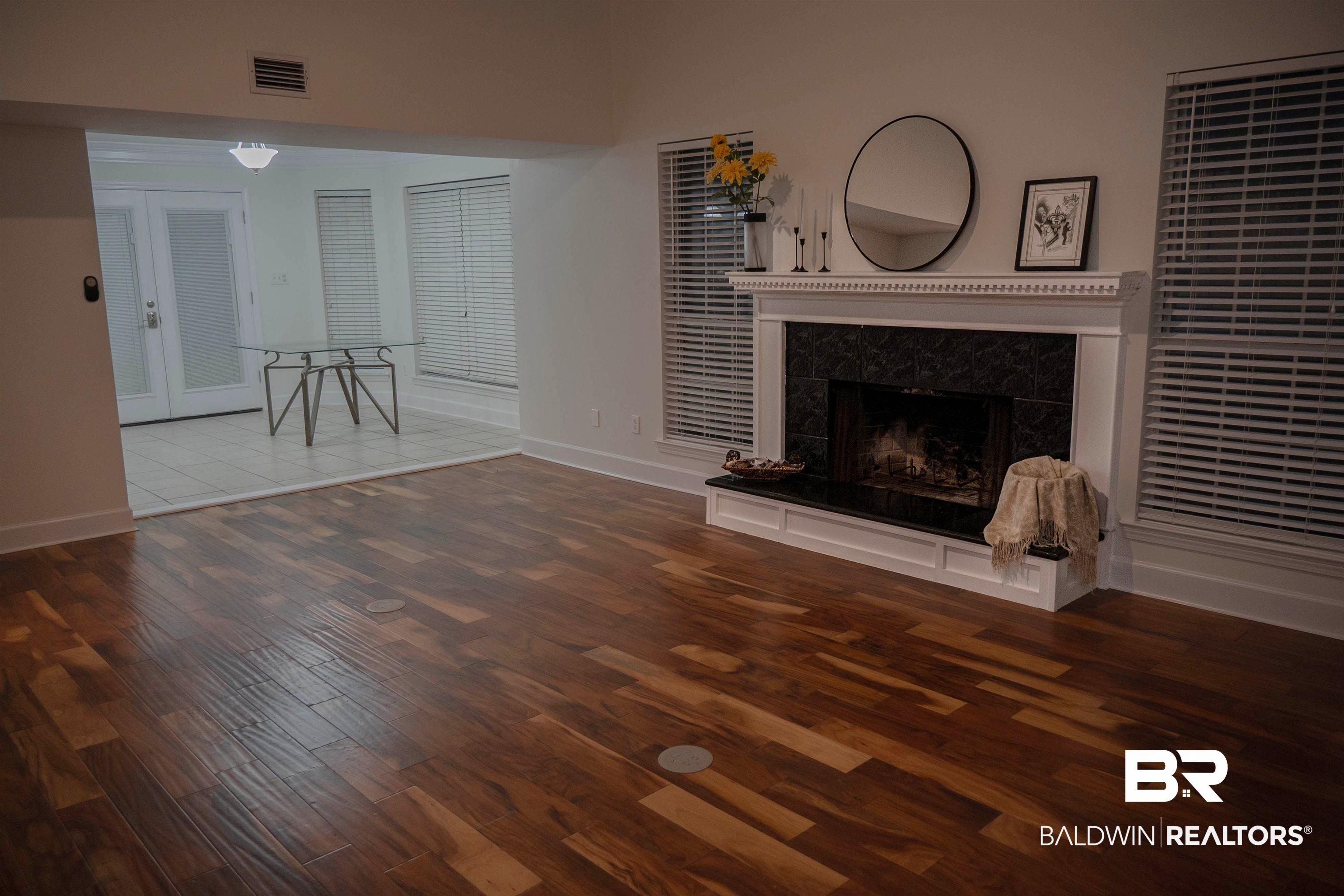 Image 3: Spacious living area featuring rich wood-finish flooring and a fireplace with a white mantel and dark stone surround