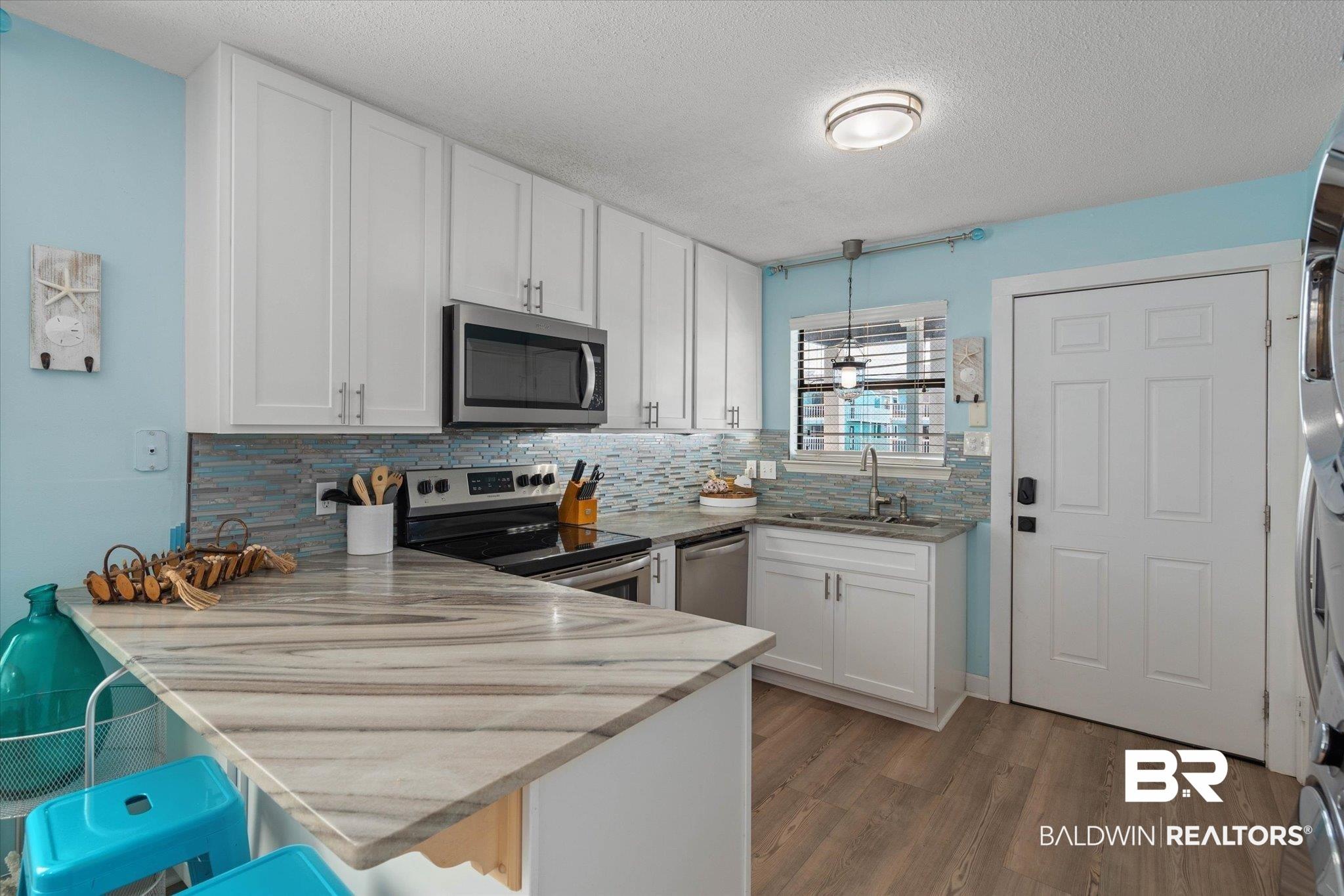 Image 4: Kitchen featuring white cabinets, a peninsula, stainless steel appliances, a breakfast bar, and a textured ceiling