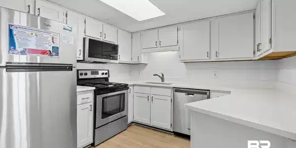 Image 3: Renovated kitchen featuring white cabinetry, light countertops, wood-finish flooring, stainless steel appliances, and a subway tile backsplash