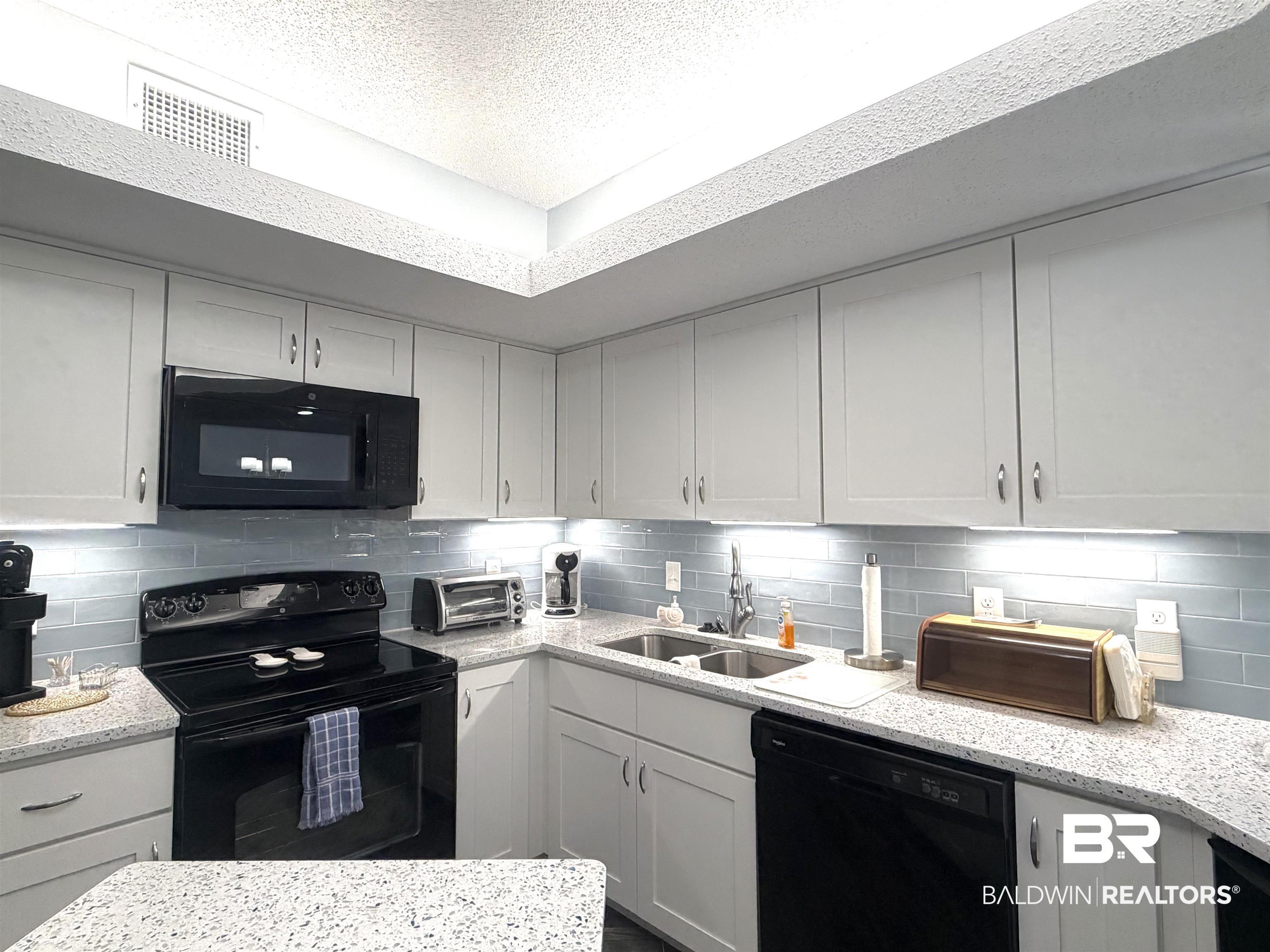 Image 3: Kitchen with black appliances, a textured ceiling, light stone countertops, white cabinetry, and tasteful backsplash