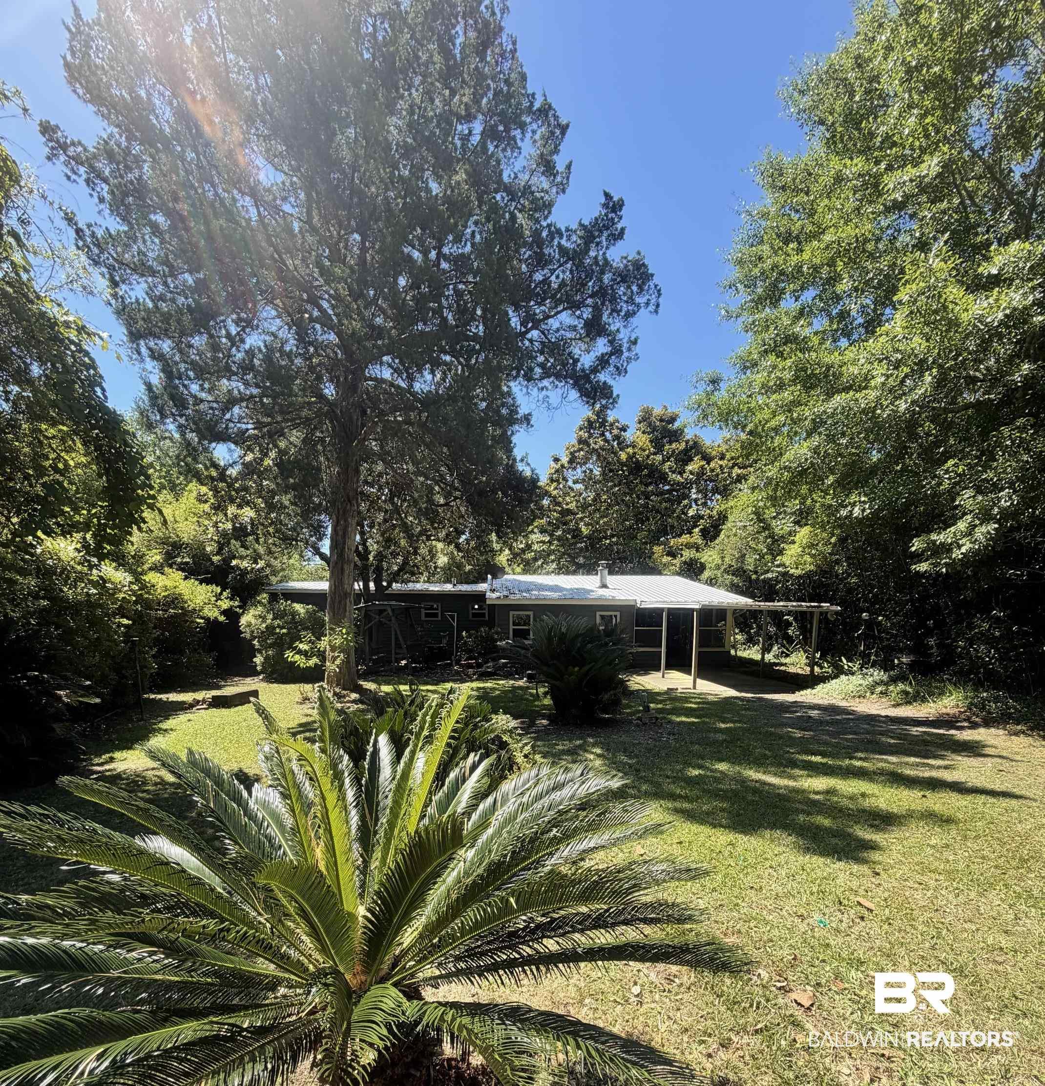Image 1: Expansive grassy yard with mature trees and established landscaping, featuring a visible portion of a single-story residence with a covered side porch