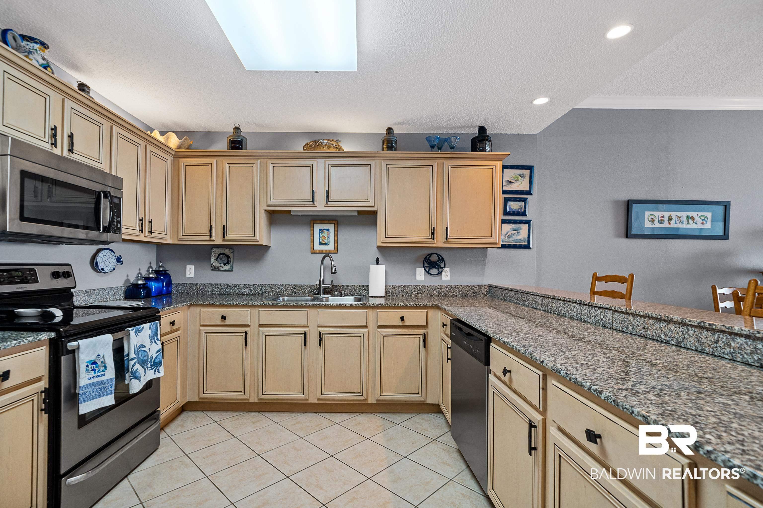 Image 4: Kitchen with appliances with stainless steel finishes, a textured ceiling, light tile patterned floors, dark stone counters, and a skylight