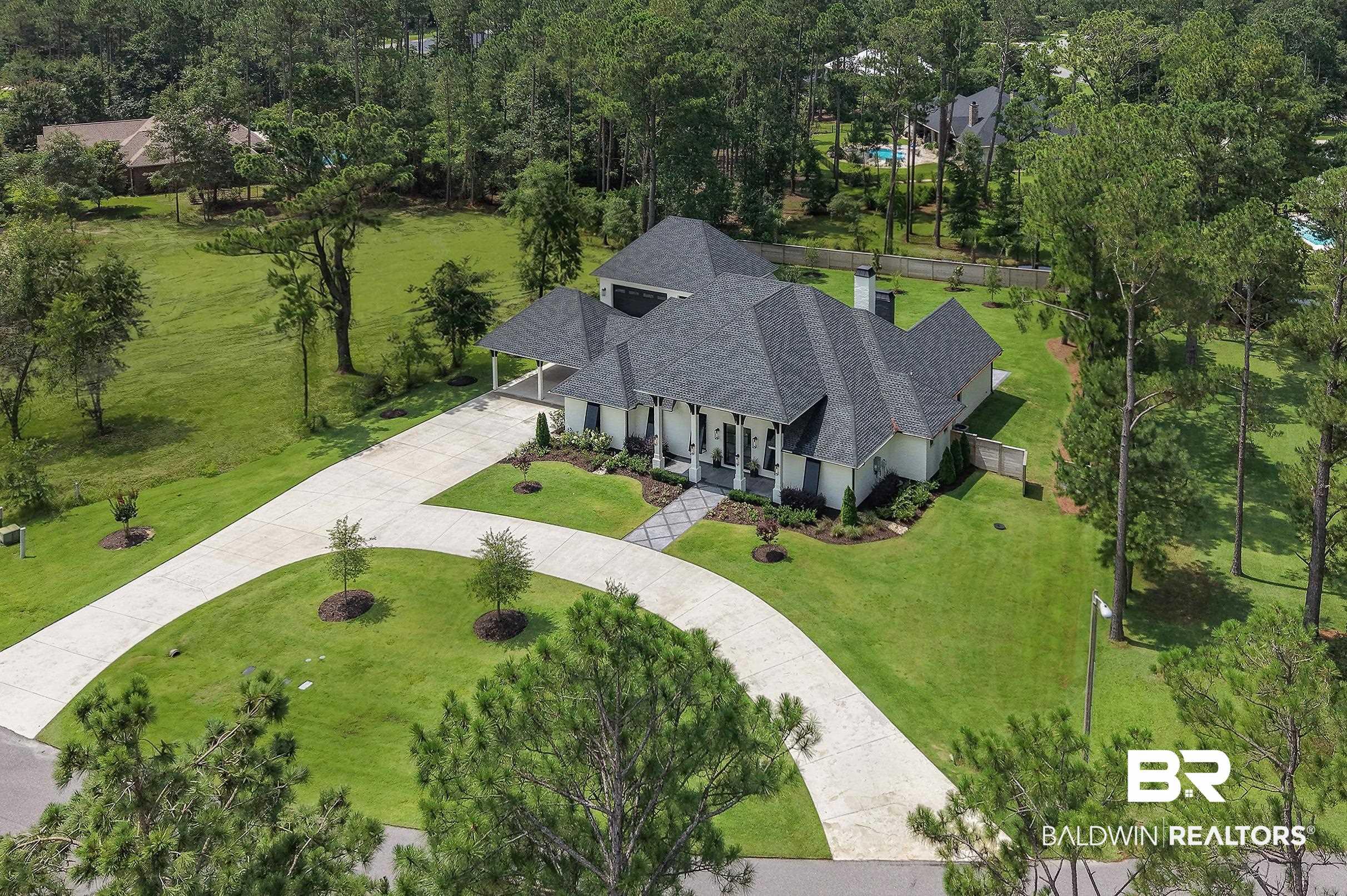 Image 2: Expansive property featuring a white exterior with dark shutters, a multi-gabled dark roof, a covered entry porch with columns, a curved concrete driveway, and mature trees surrounding the perimeter