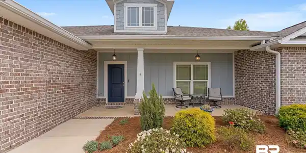Image 4: View of exterior entry with a shingled roof, covered porch, board and batten siding, and brick siding