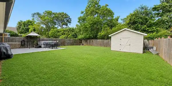 Image 2: Expansive backyard featuring a large green lawn, concrete patio, privacy fencing, and a detached storage shed