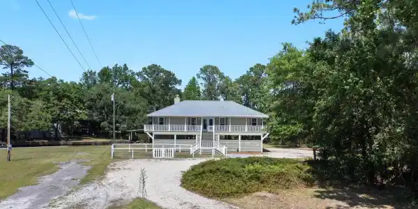 Image 2: Elevated home featuring a light green exterior, white railings, and a gray metal roof