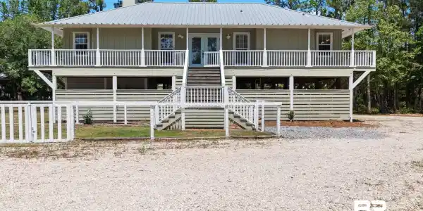 Image 4: Elevated residence featuring a metal roof, a full-width covered porch with white railings, and light green horizontal siding
