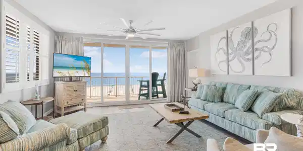 Image 3: Open-concept living area featuring a full wall of glass sliders opening to a balcony with water and beach scenery