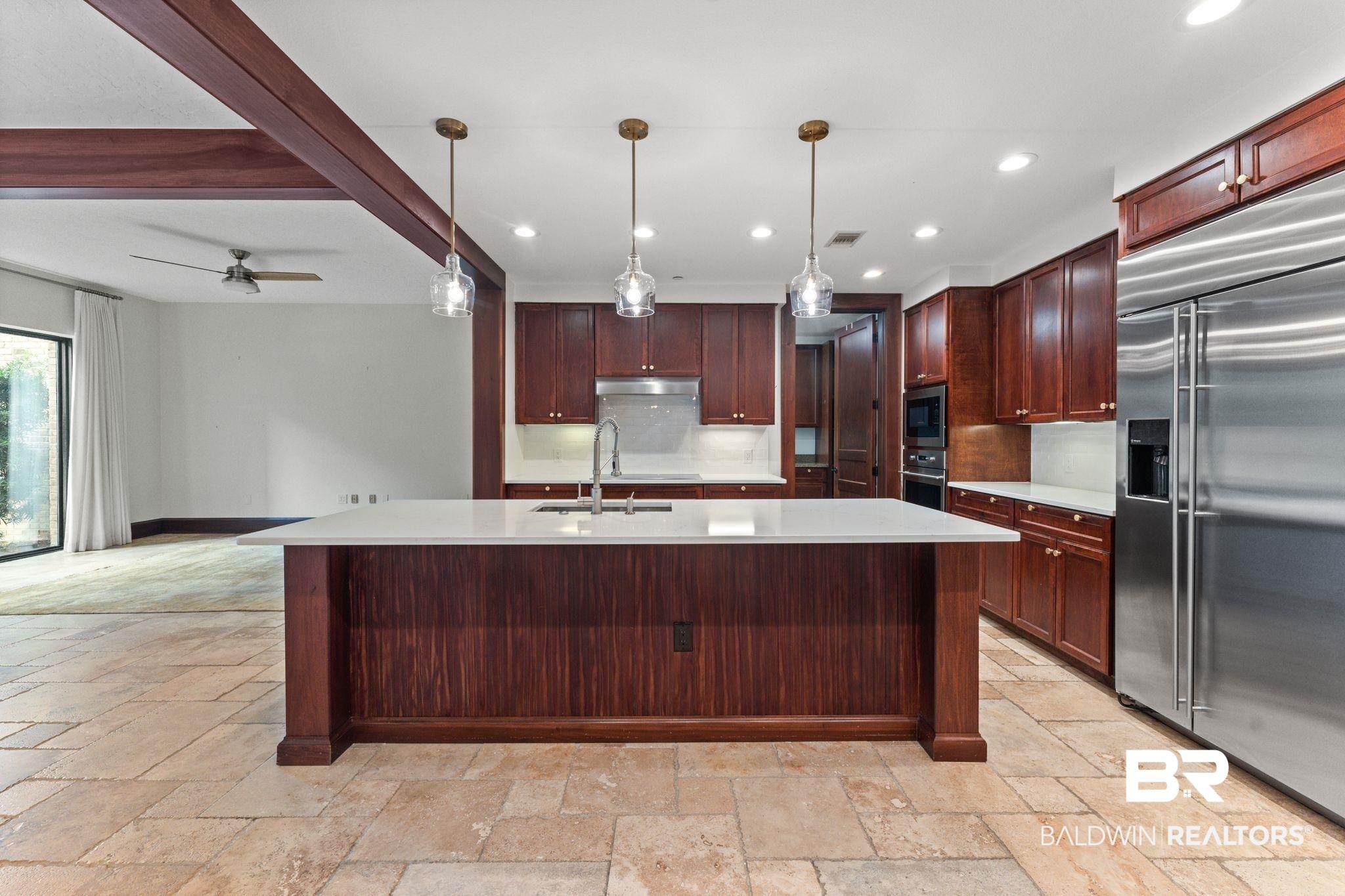 Image 2: Kitchen with built in appliances, hanging light fixtures, beam ceiling, a center island with sink, and stone tile floors