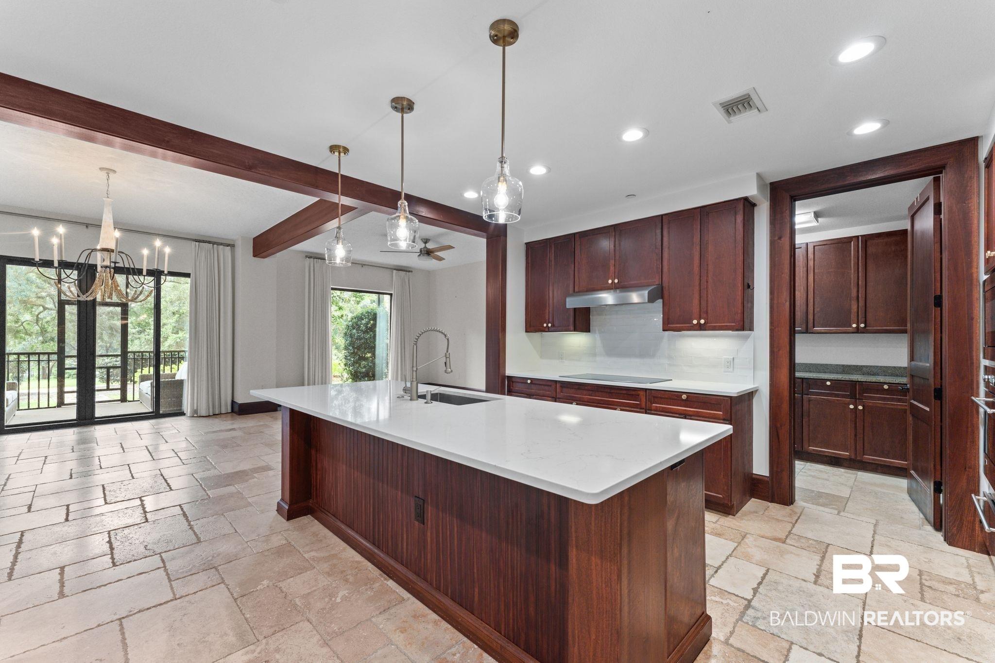 Image 3: Kitchen featuring beamed ceiling, light stone counters, hanging light fixtures, recessed lighting, and a kitchen island with sink