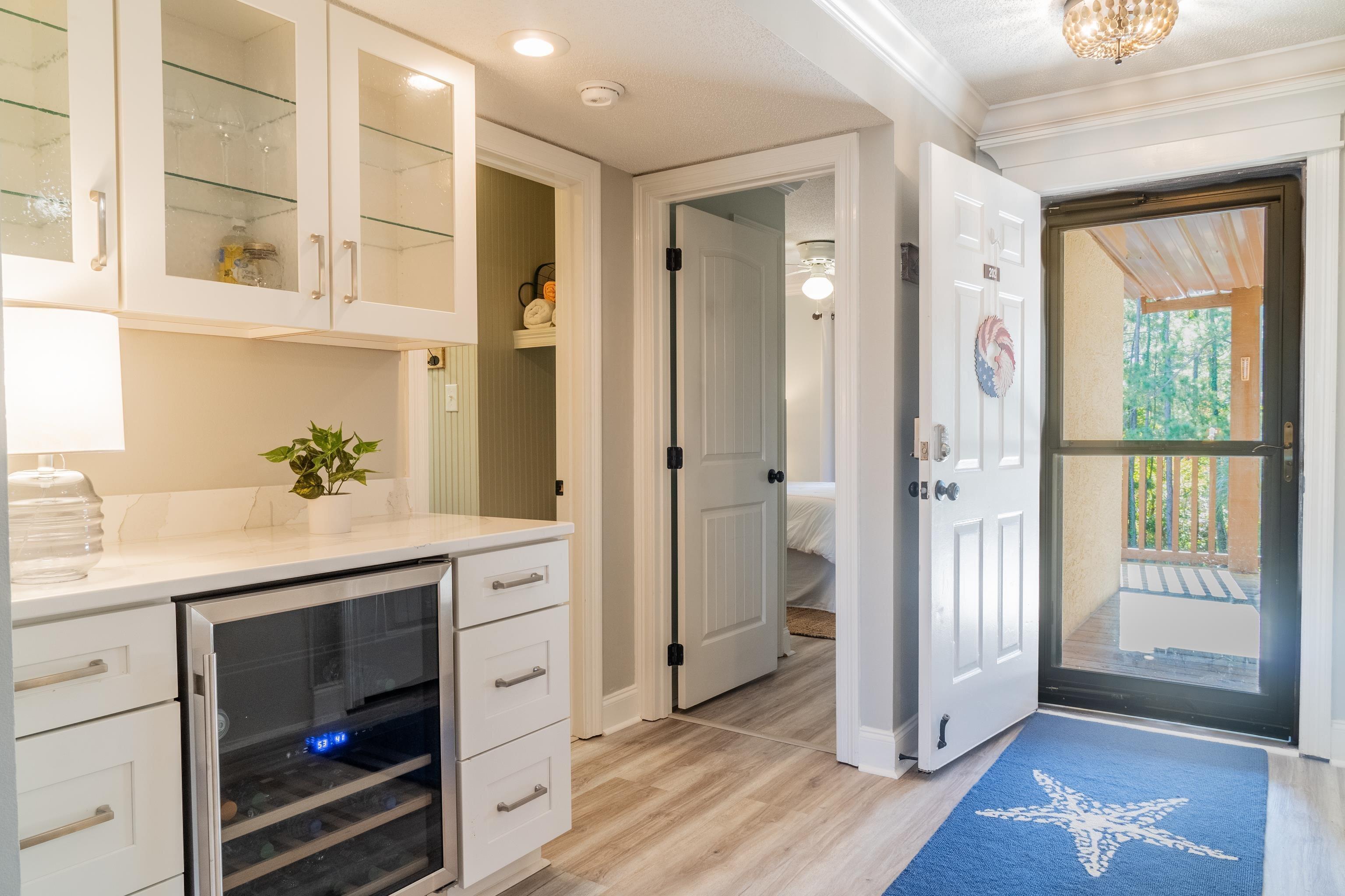 Image 2: Bar featuring glass insert cabinets, white cabinetry, beverage cooler, light stone countertops, and light wood-style flooring