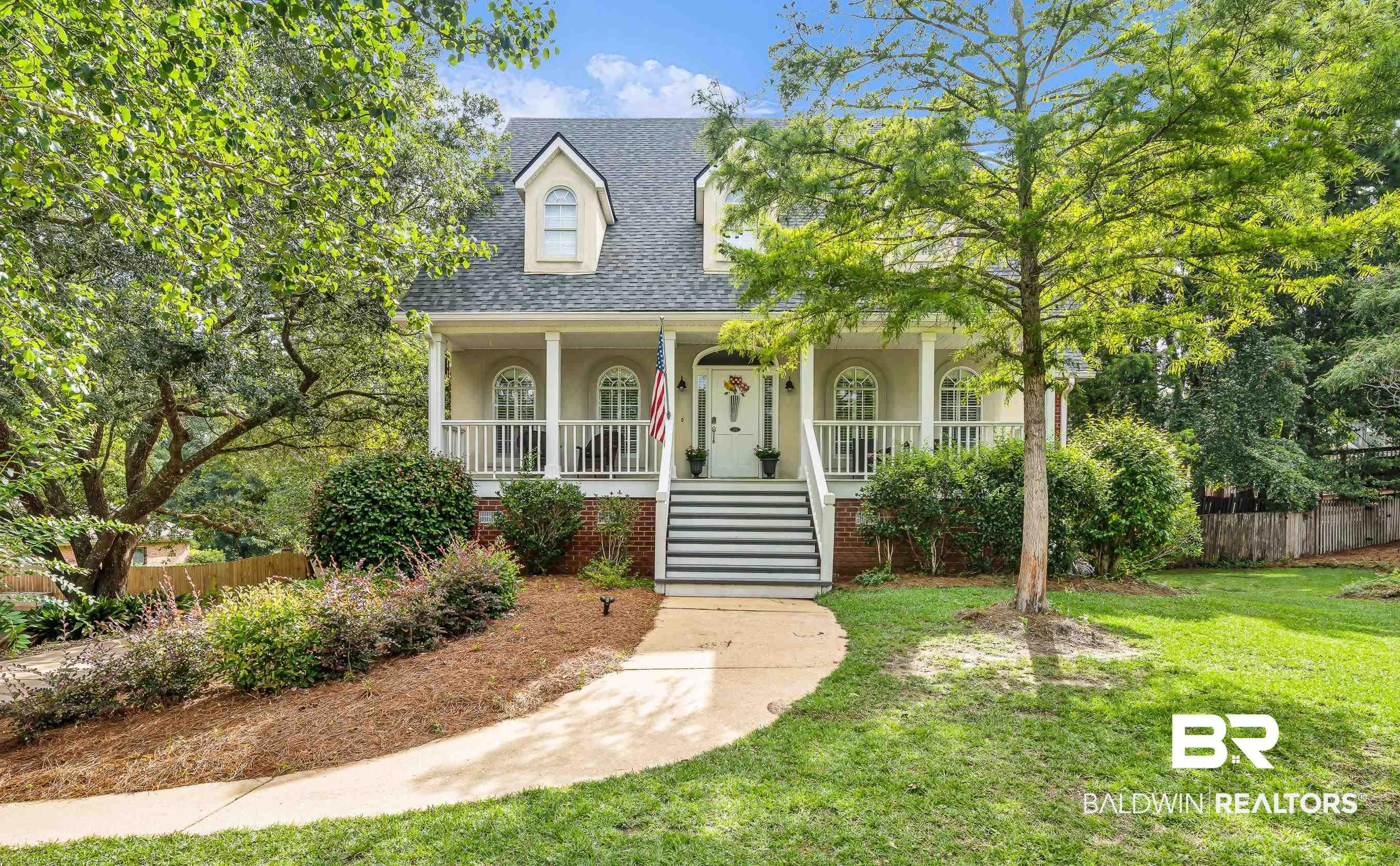 Image 2: Two-story residence featuring a covered front porch with white columns and railings, dormer windows, a gabled roof, and a brick foundation