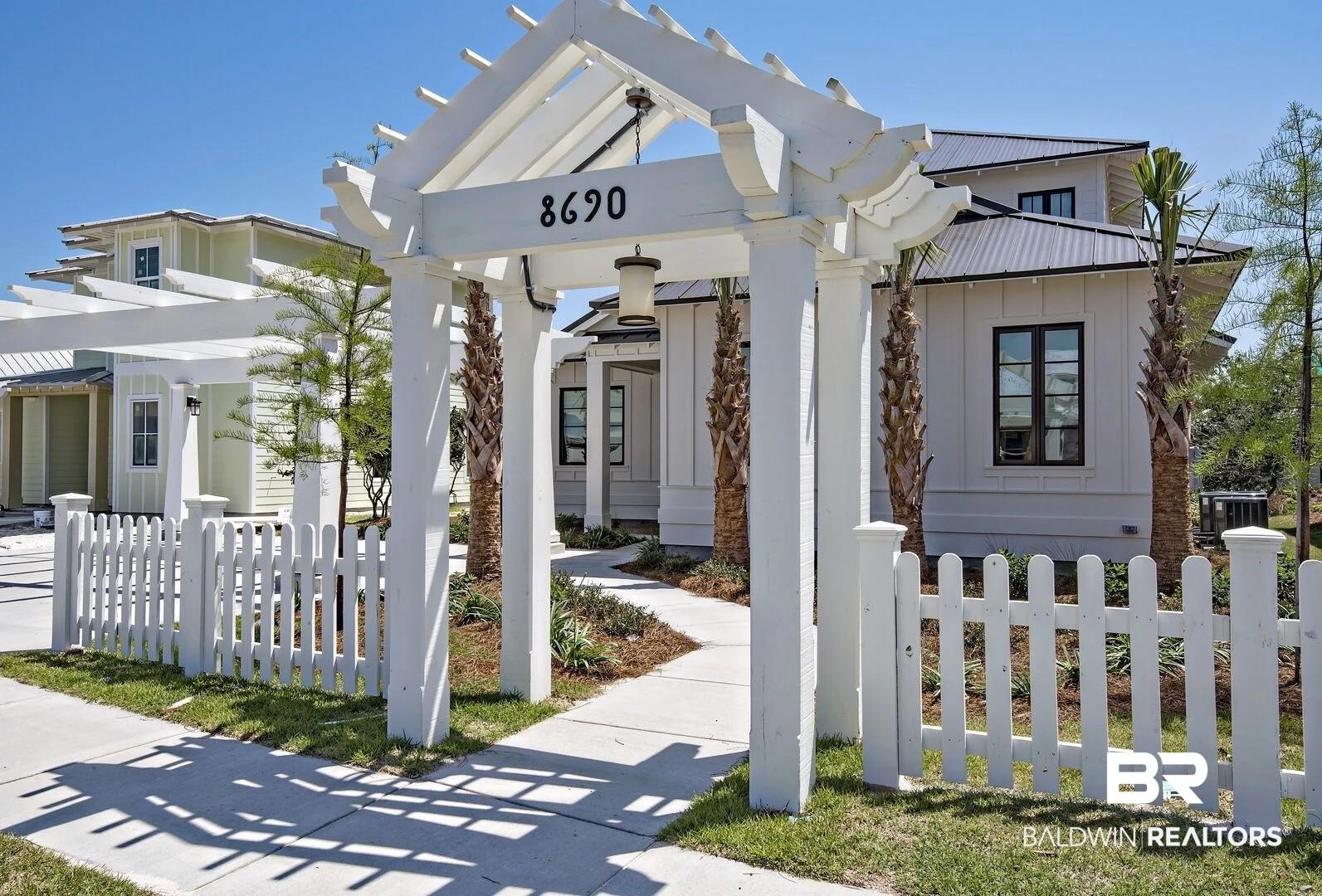 Image 2: White picket fence and pergola entrance leading to a residence with board and batten siding, black-framed windows, and a metal roof