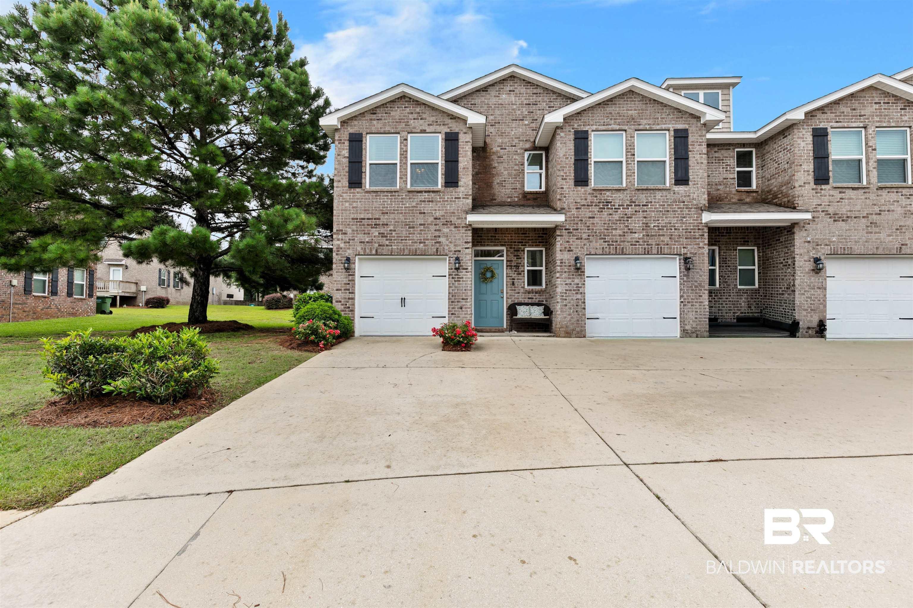 Image 1: Brick facade townhouse featuring a light blue entry door, individual garage, and black louvered shutters