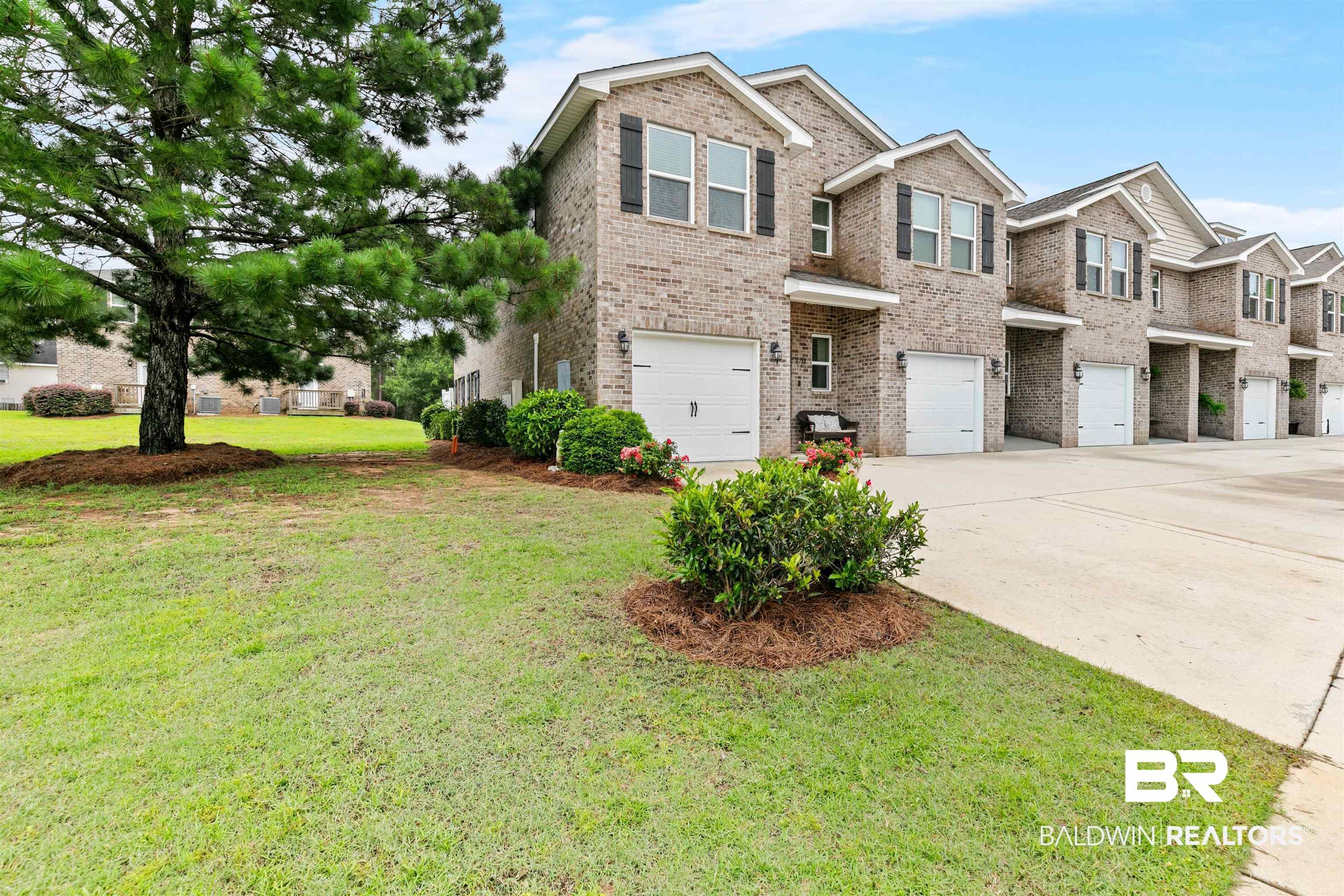 Image 2: Brick exterior townhome featuring an attached garage, landscaped shrubbery, and a paved driveway