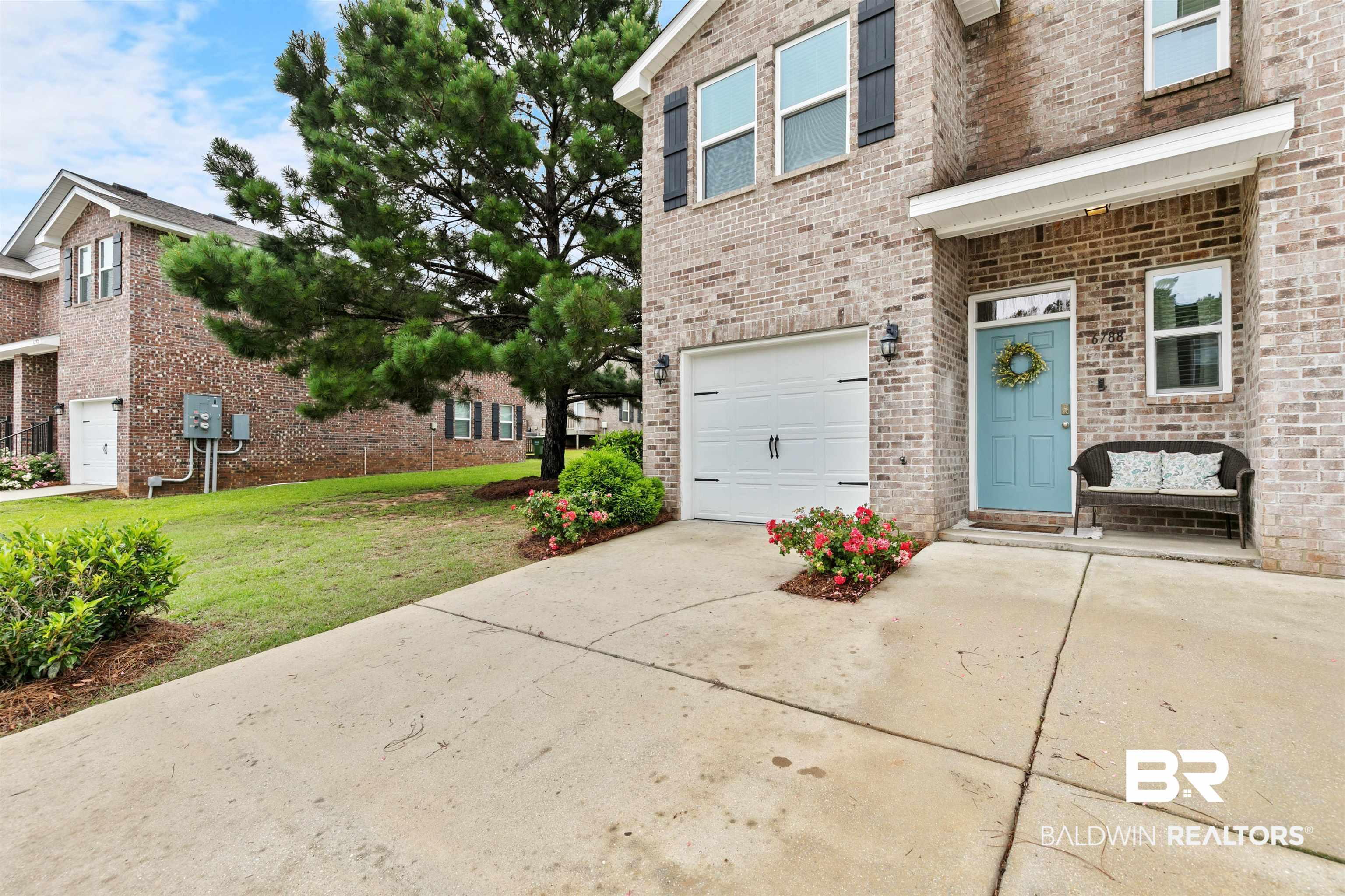 Image 3: Brick exterior featuring a light blue entry door, an attached garage, and a concrete driveway