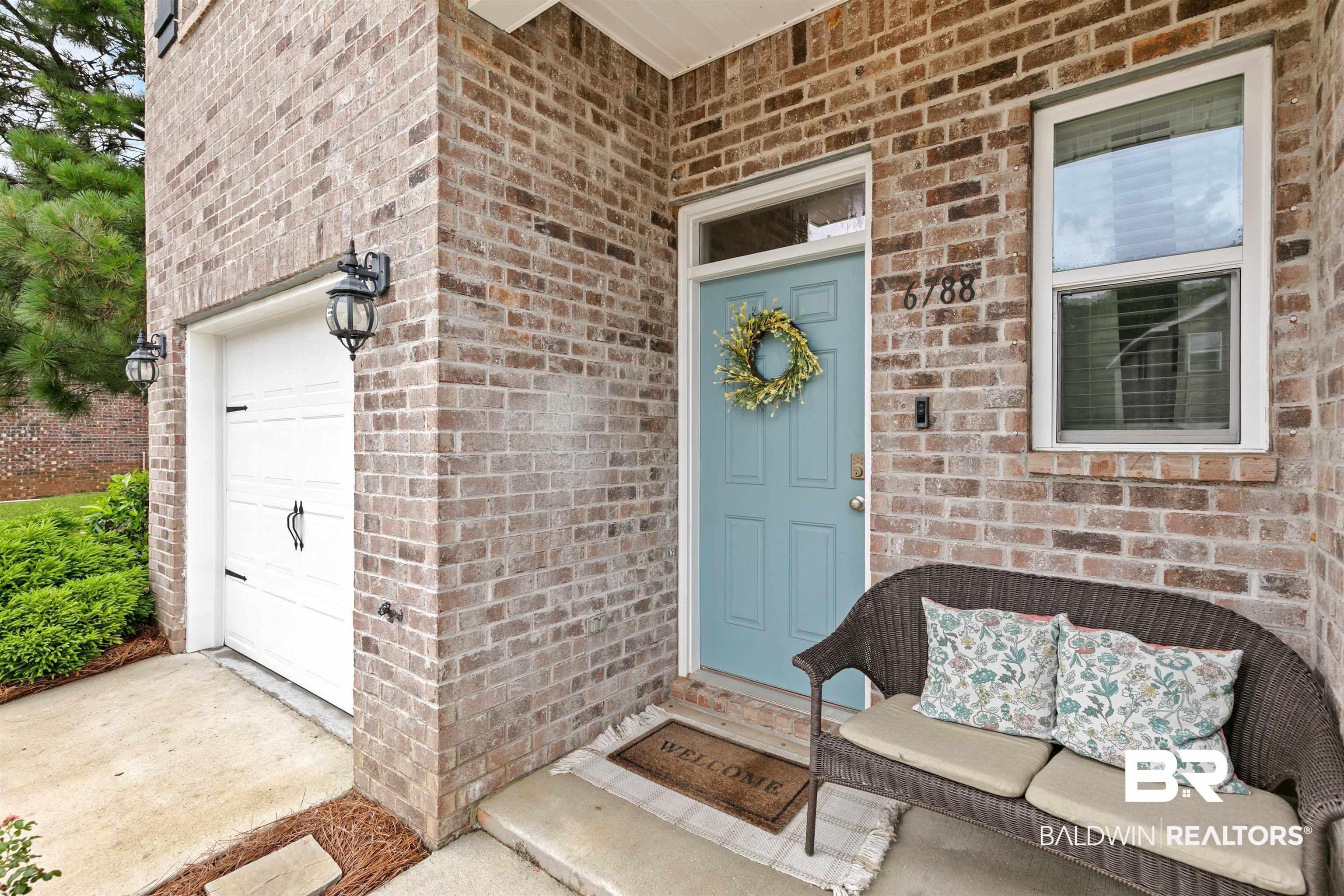Image 4: Brick exterior featuring a light blue front door with transom window, an adjacent single-pane window, and an attached single-car garage with overhead lighting