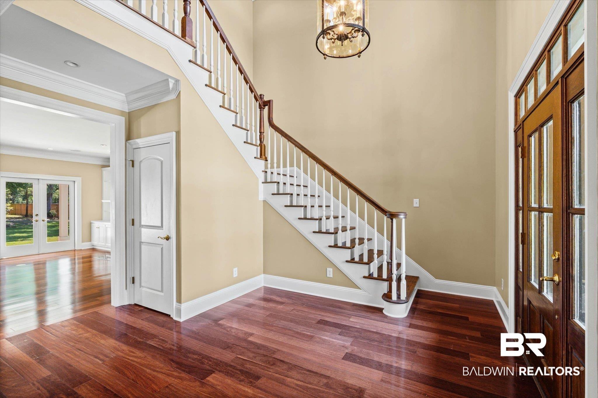 Image 3: Two-story entryway featuring a grand staircase with dark wood-finish treads and handrail, white balusters, and a decorative chandelier
