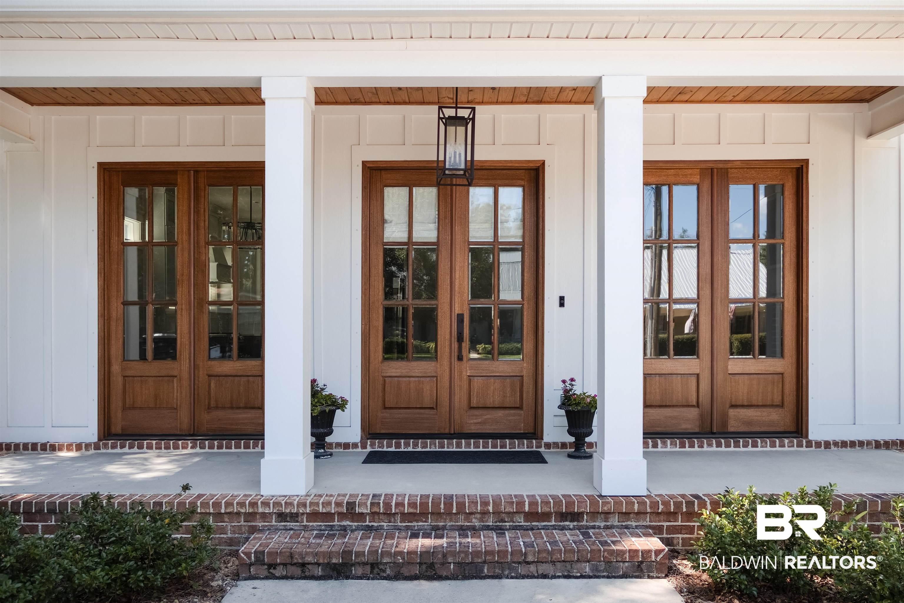 Image 3: Entryway featuring a pair of wood-finish double doors with clear glass panes, flanked by an additional wood-finish door with clear glass