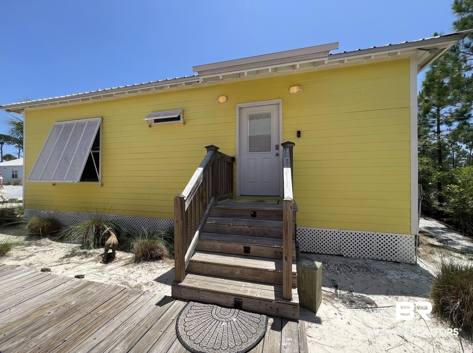 Image 2: Yellow clapboard siding with a light gray entry door, wood steps, and a wooden deck