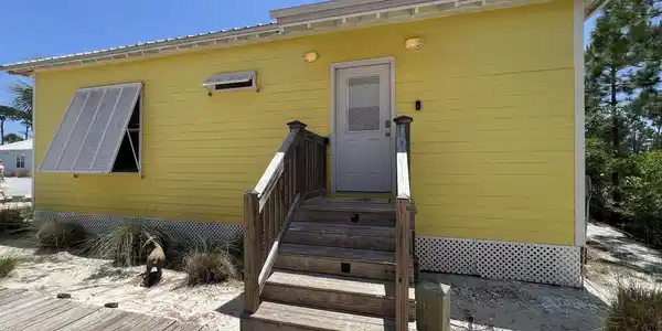 Image 2: Yellow clapboard siding with a light gray entry door, wood steps, and a wooden deck