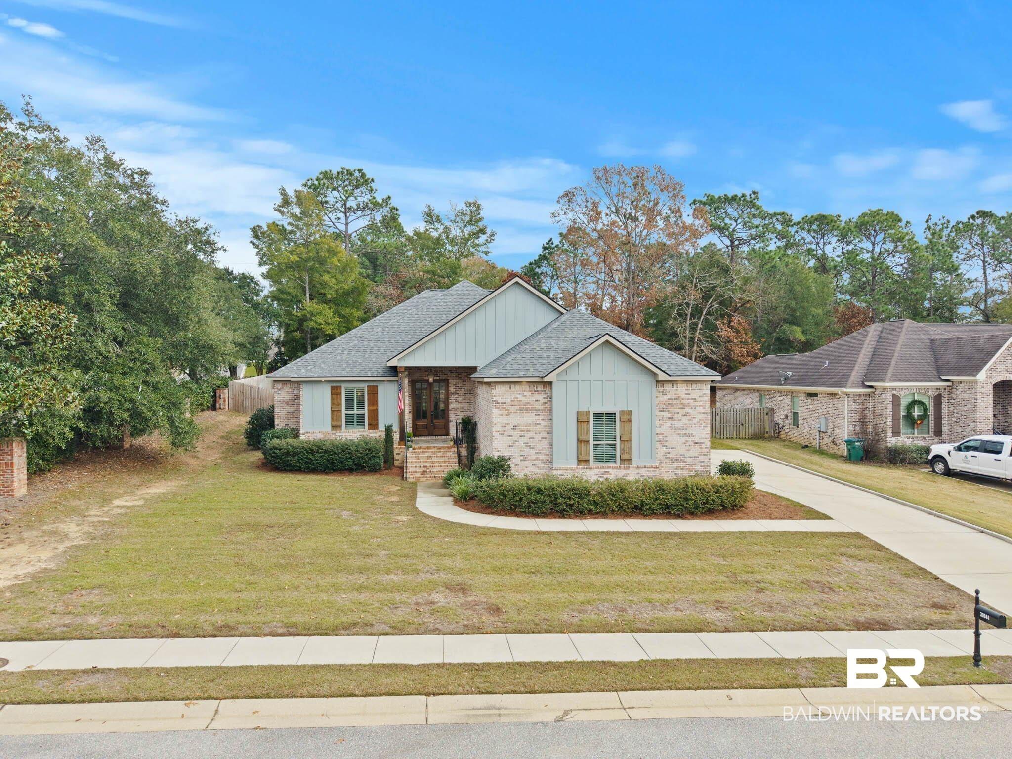 Image 3: View of front of property with board and batten siding, brick siding, driveway, and view of wooded area