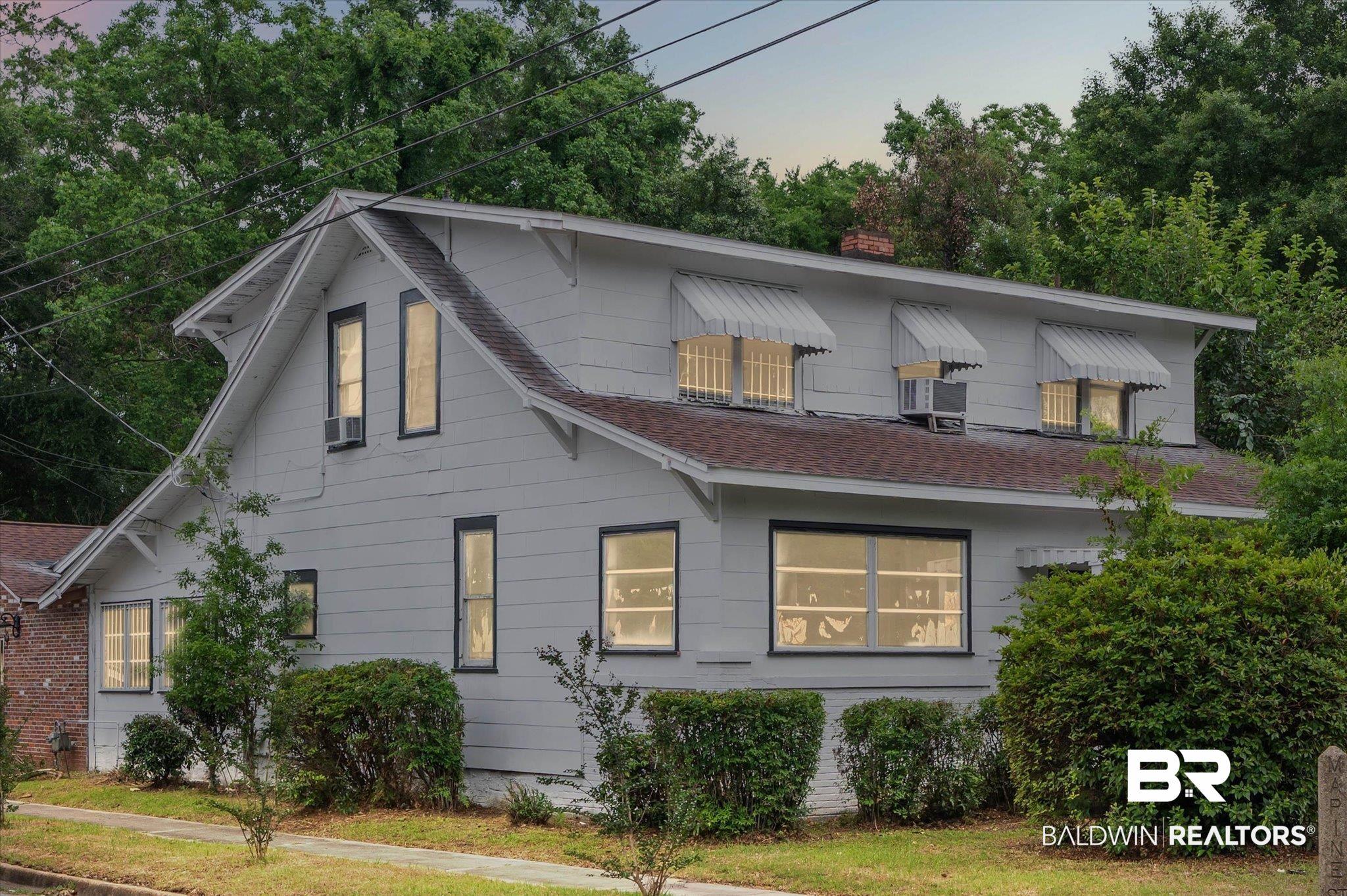 Image 2: Two-story property featuring a light gray exterior siding, dark trim windows, and a brown shingle roof