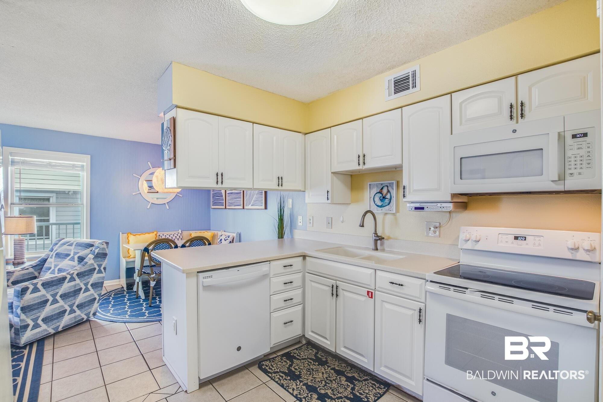 Image 3: Kitchen featuring white cabinetry, a flat-top electric range, a built-in microwave, a dishwasher, and a double basin sink