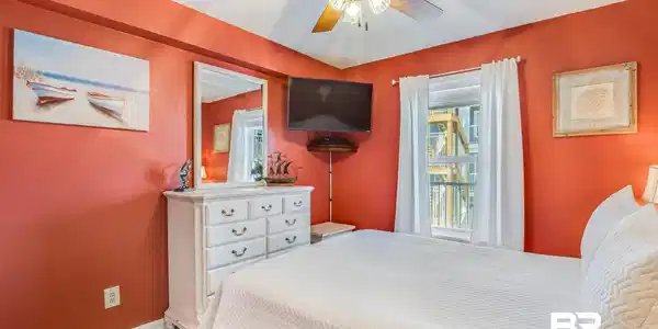 Image 4: Bedroom featuring a ceiling fan with integrated lighting, a wall-mounted television, and a window with white curtains