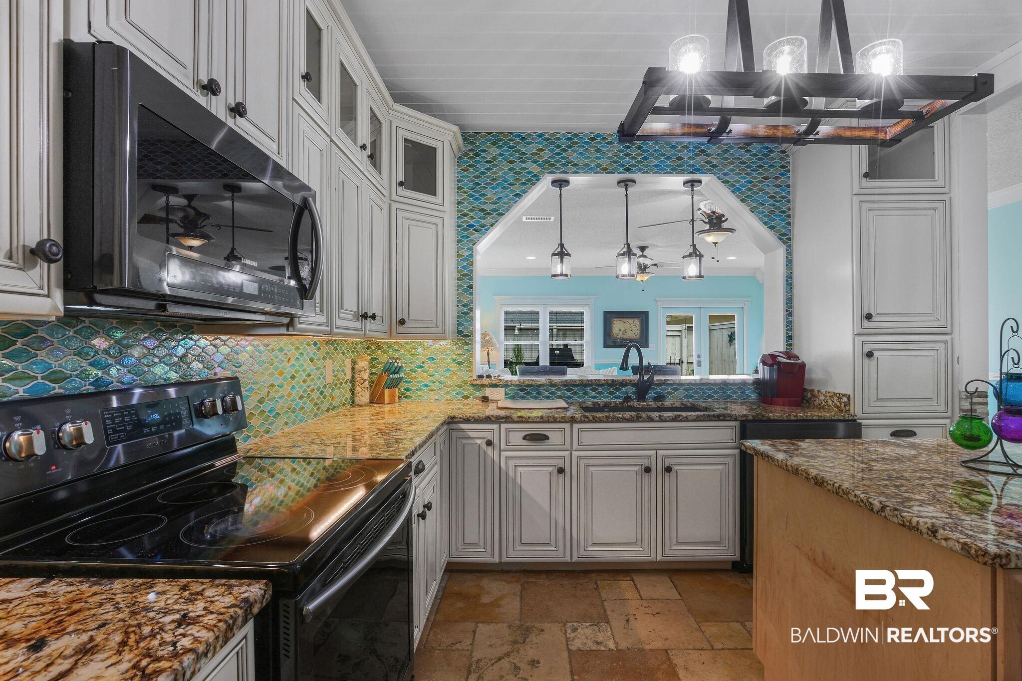 Image 4: Kitchen featuring white shaker-style cabinetry, granite countertops, and a blue and green glass tile backsplash