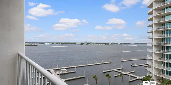 Image 2: Waterfront balcony with white railing, featuring extensive marina docks, a body of water, distant land, and a portion of a curving multi-story building