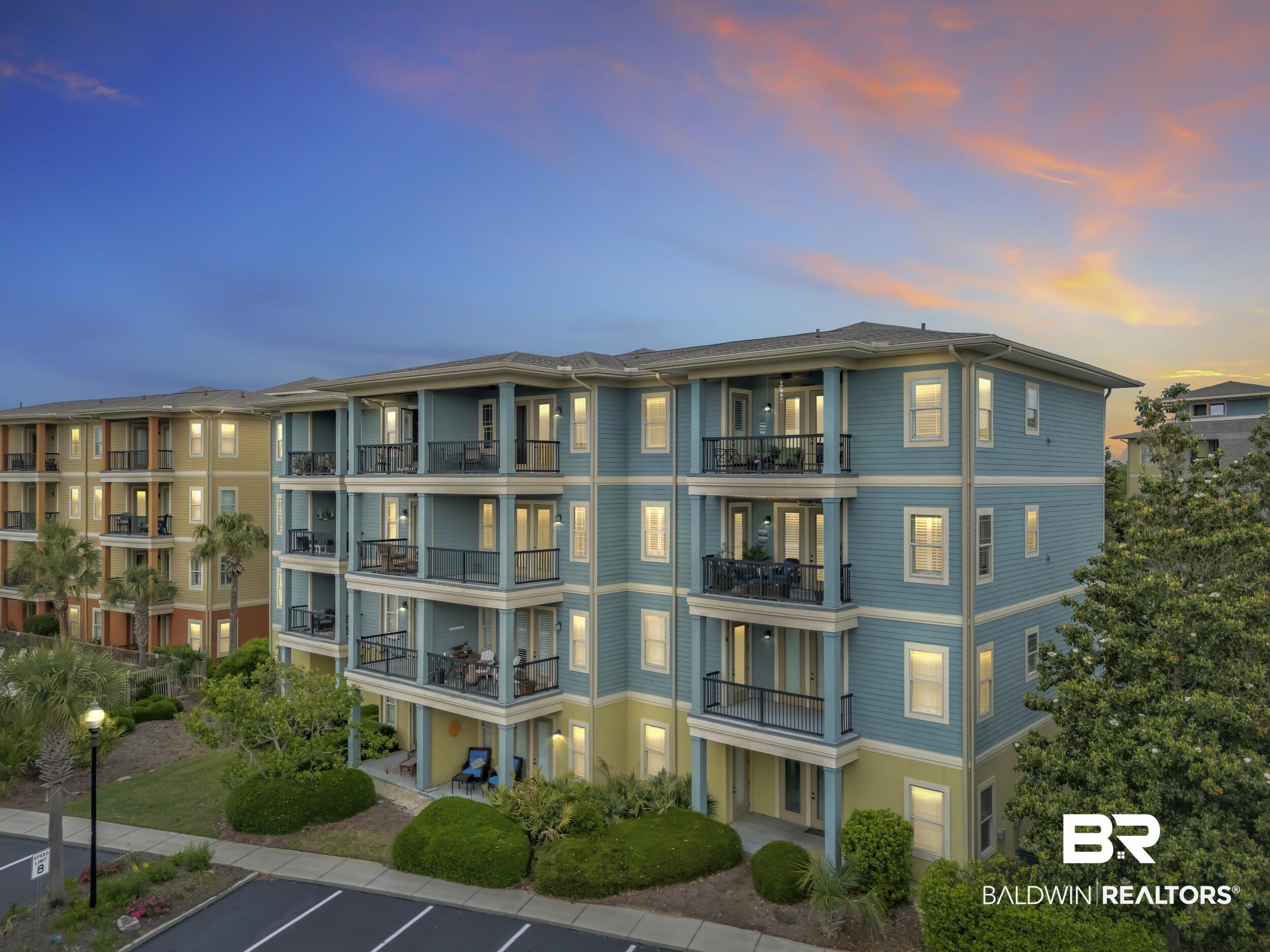 Image 2: Multi-story building featuring individual balconies with black railings, a light blue and yellow exterior, and surrounding green landscaping