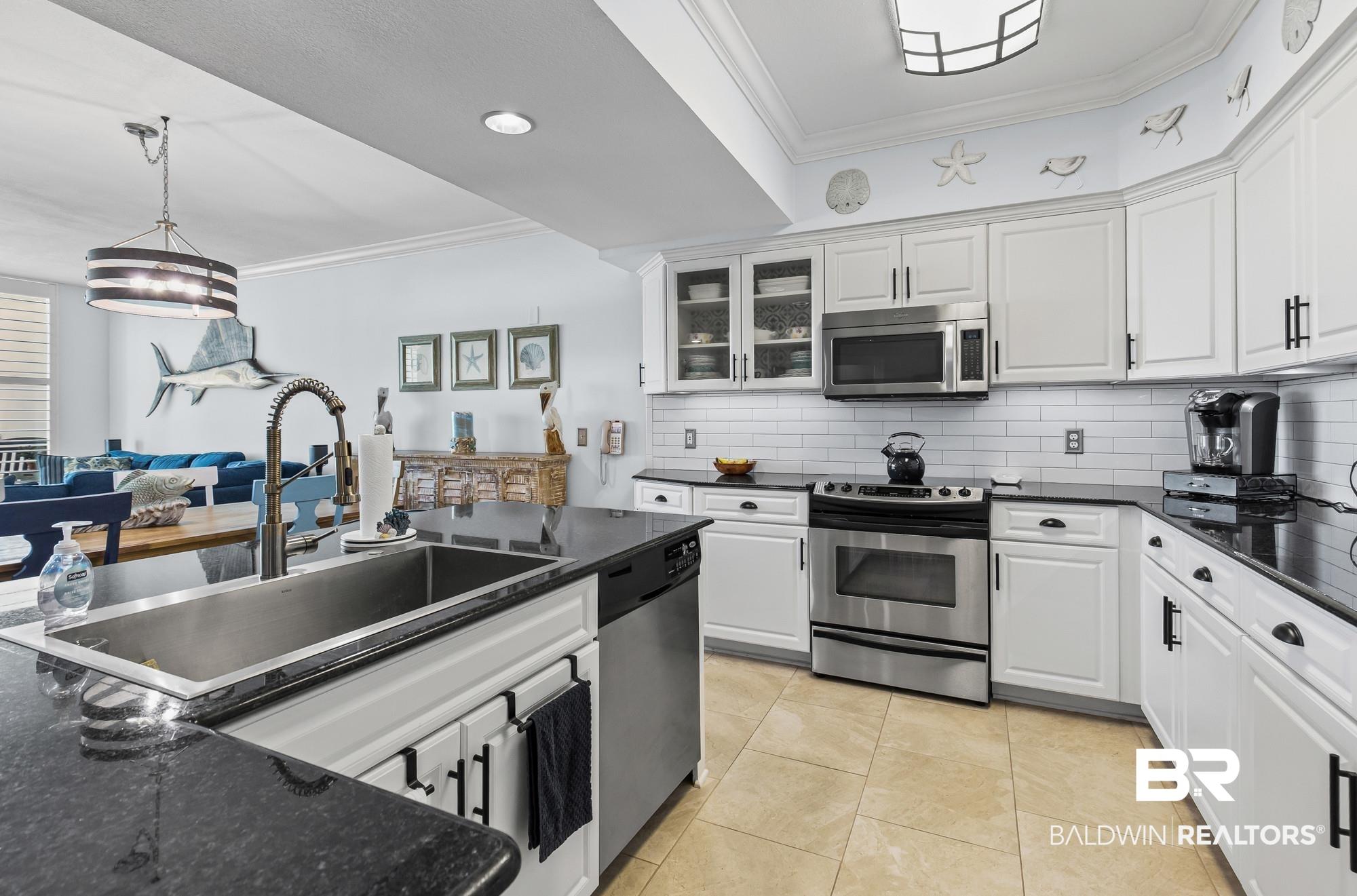 Image 2: Open-concept kitchen featuring white cabinetry, dark stone countertops, stainless steel appliances, a subway tile backsplash, and tile flooring