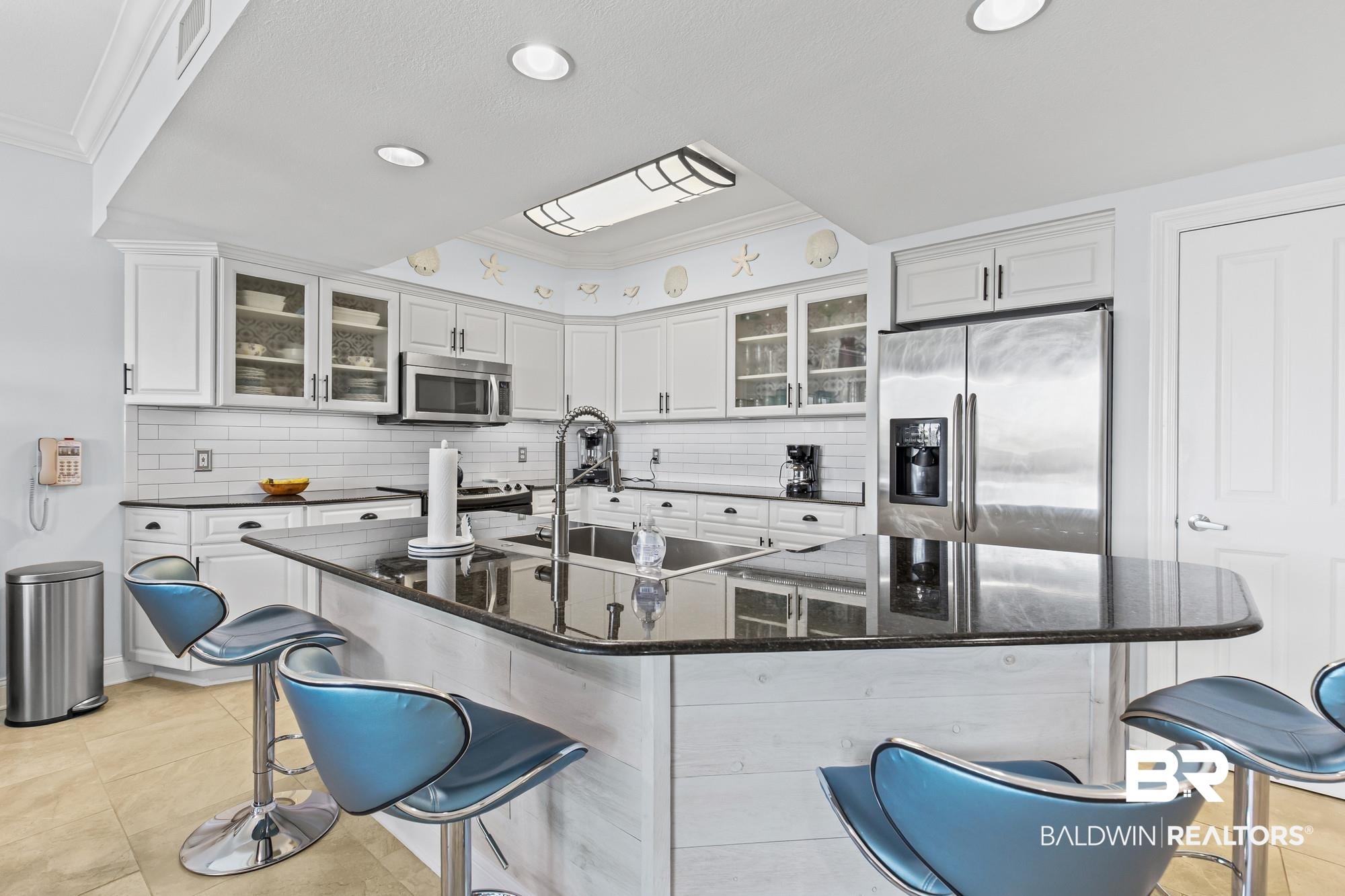 Image 3: Kitchen featuring white cabinetry, subway tile backsplash, stainless steel appliances, a center island with a dark countertop, and recessed lighting