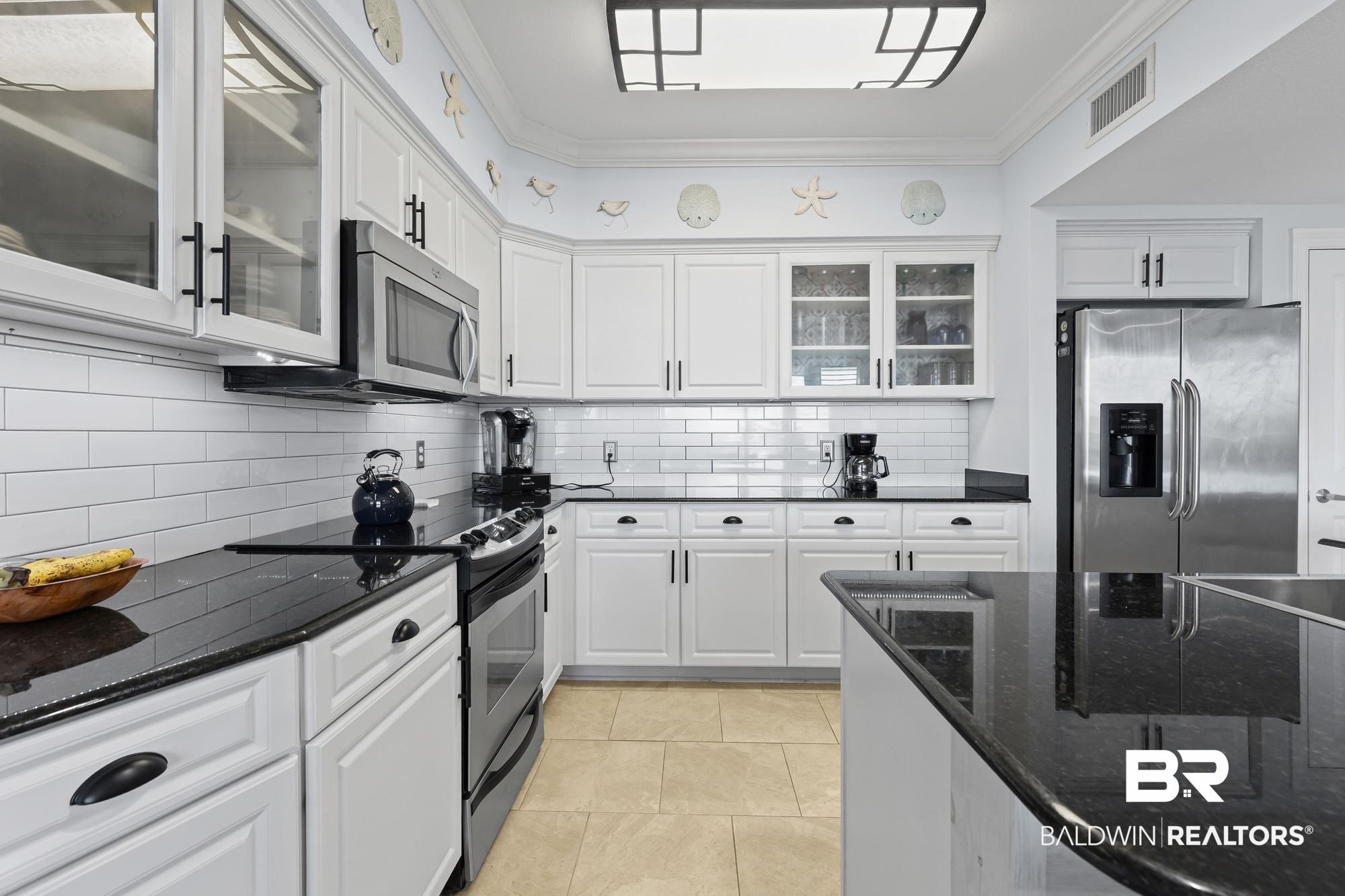 Image 4: Kitchen featuring white cabinetry, black stone countertops, stainless steel appliances, a subway tile backsplash, and light-toned tile flooring
