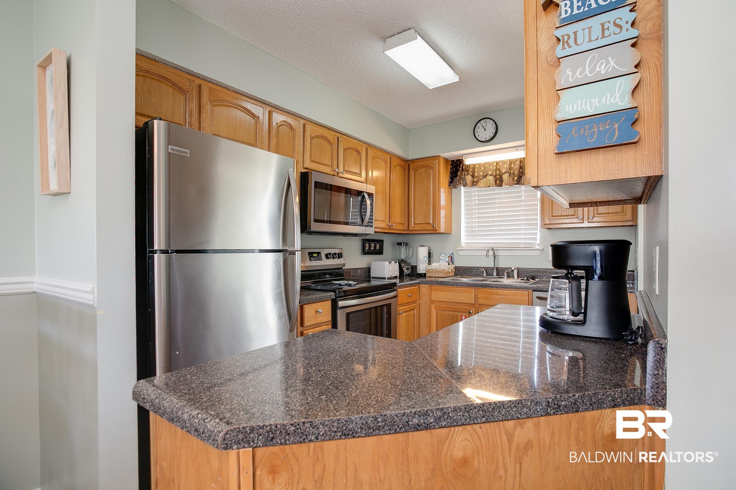 Image 2: Kitchen with stainless steel appliances, a peninsula, a textured ceiling, and brown cabinetry