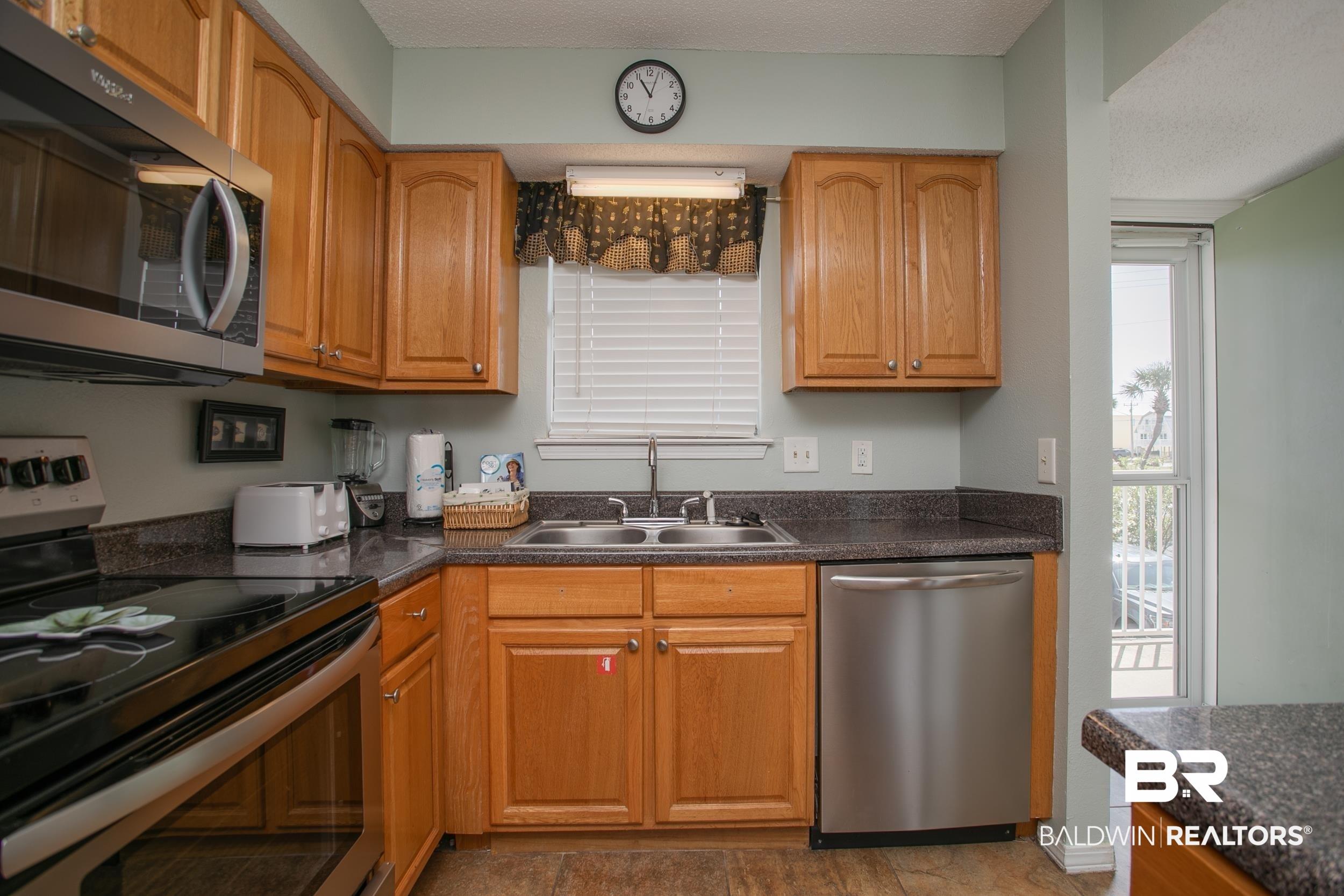 Image 3: Kitchen with stainless steel appliances, dark countertops, and brown cabinetry