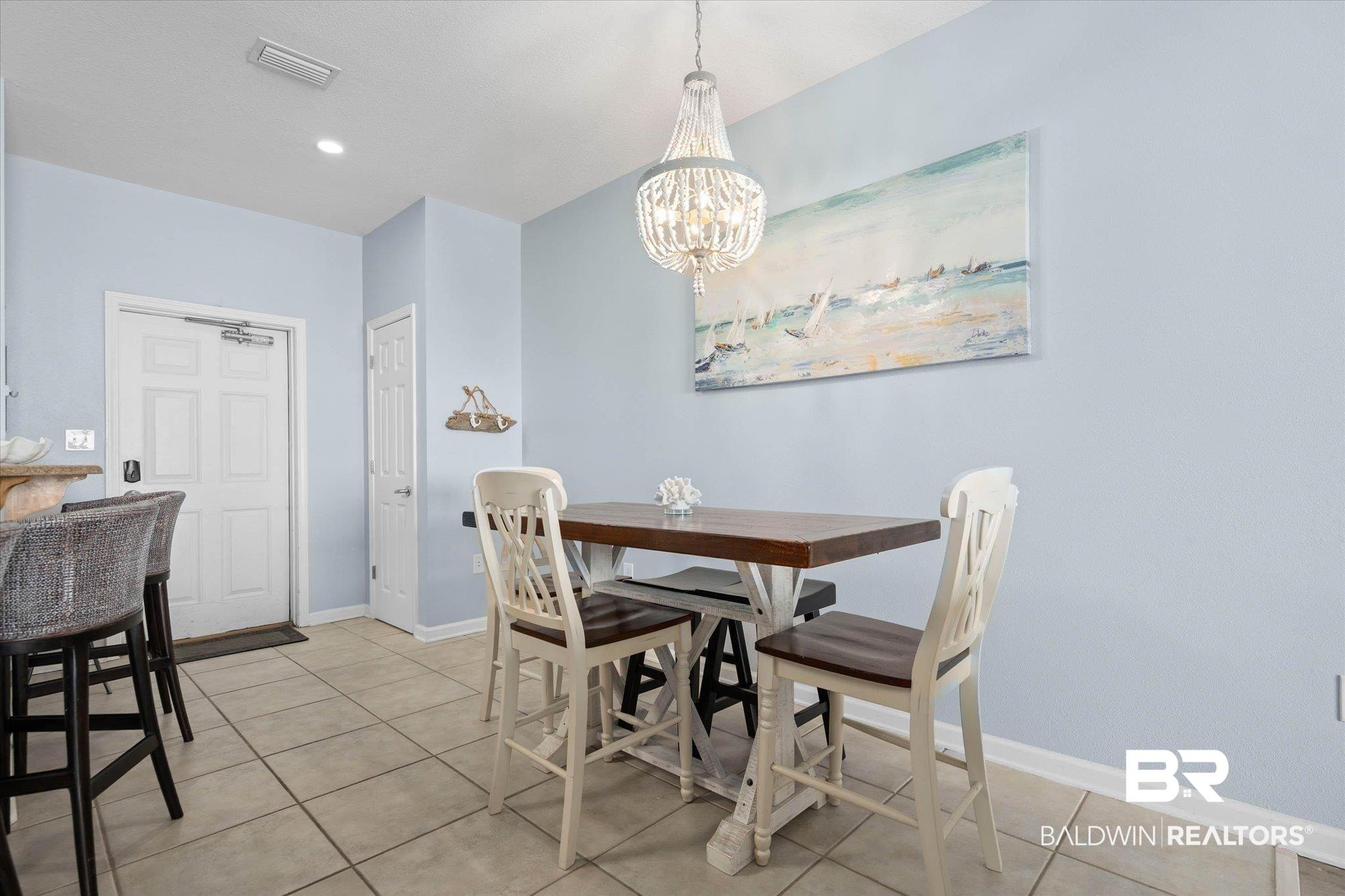Image 3: Casual dining area featuring a crystal chandelier, light blue wall paint, and tile flooring