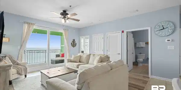 Image 4: Living area featuring expansive glass sliding doors opening to a balcony, wood-finish flooring, a ceiling fan with integrated lighting, and light blue wall paint