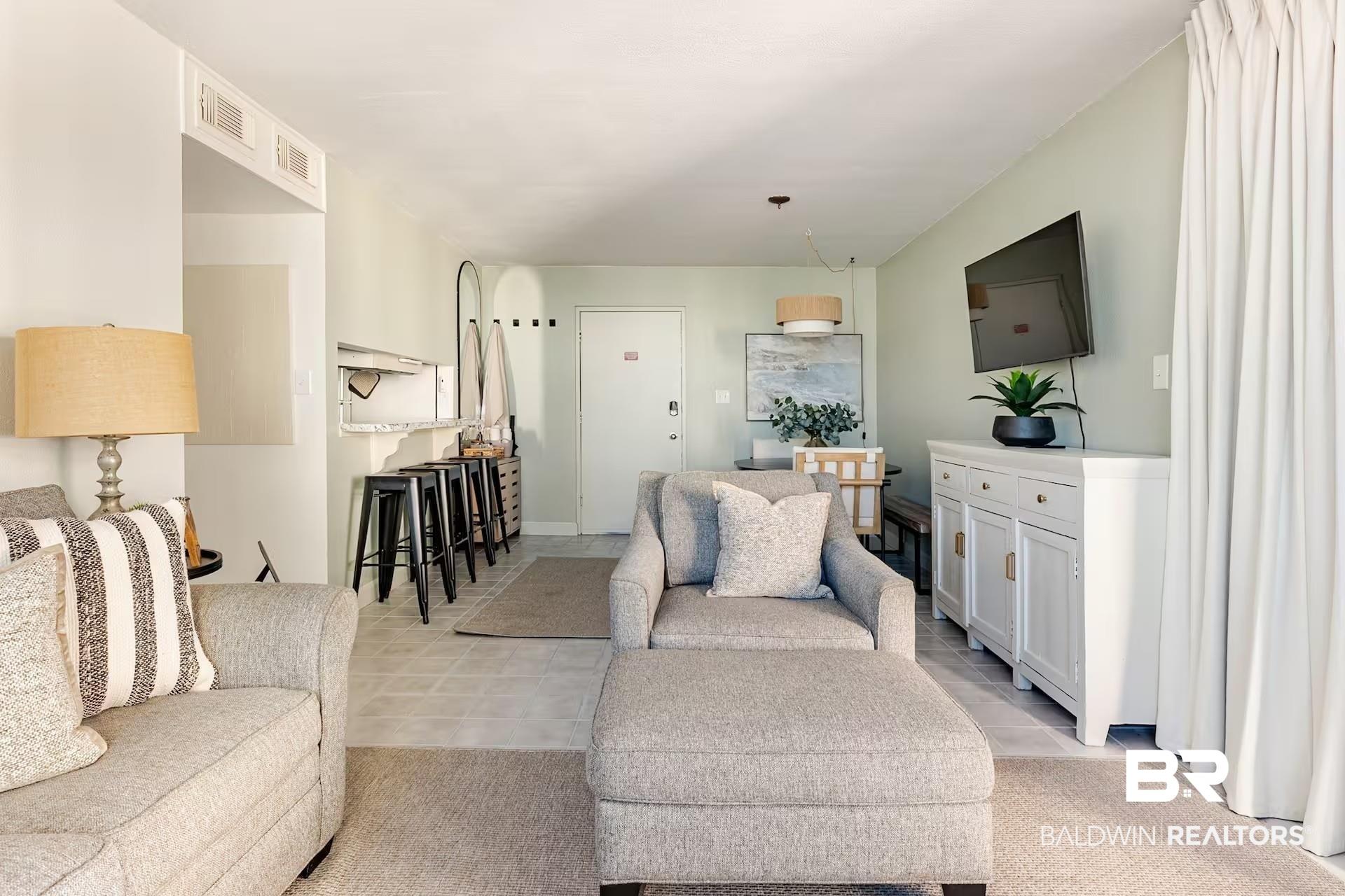 Image 4: Open-concept living area featuring light-toned flooring, a light green accent wall, and white drapery
